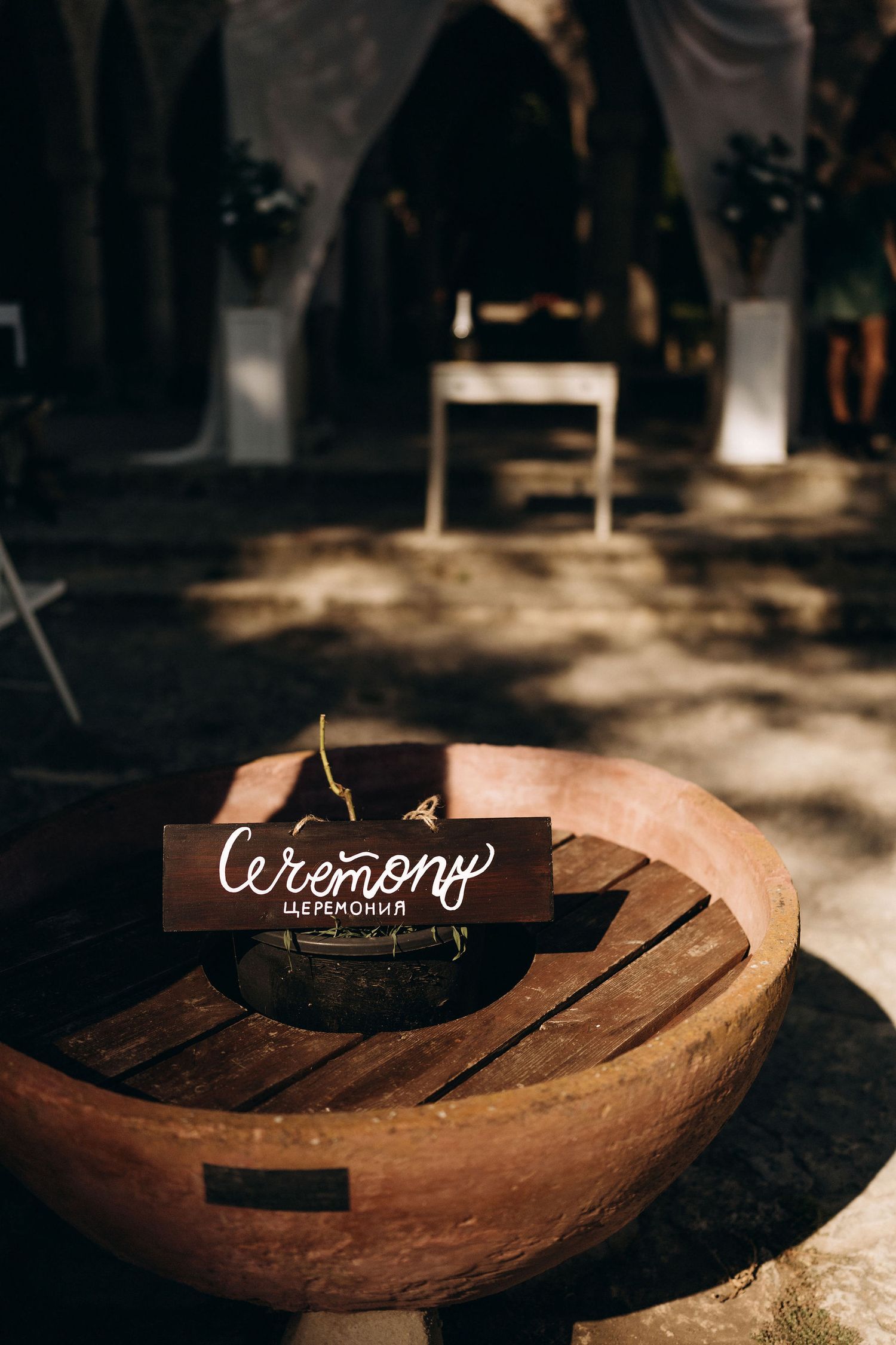 Wooden sign reading 'Ceremony' placed on a rustic circular table in a shadowy venue.