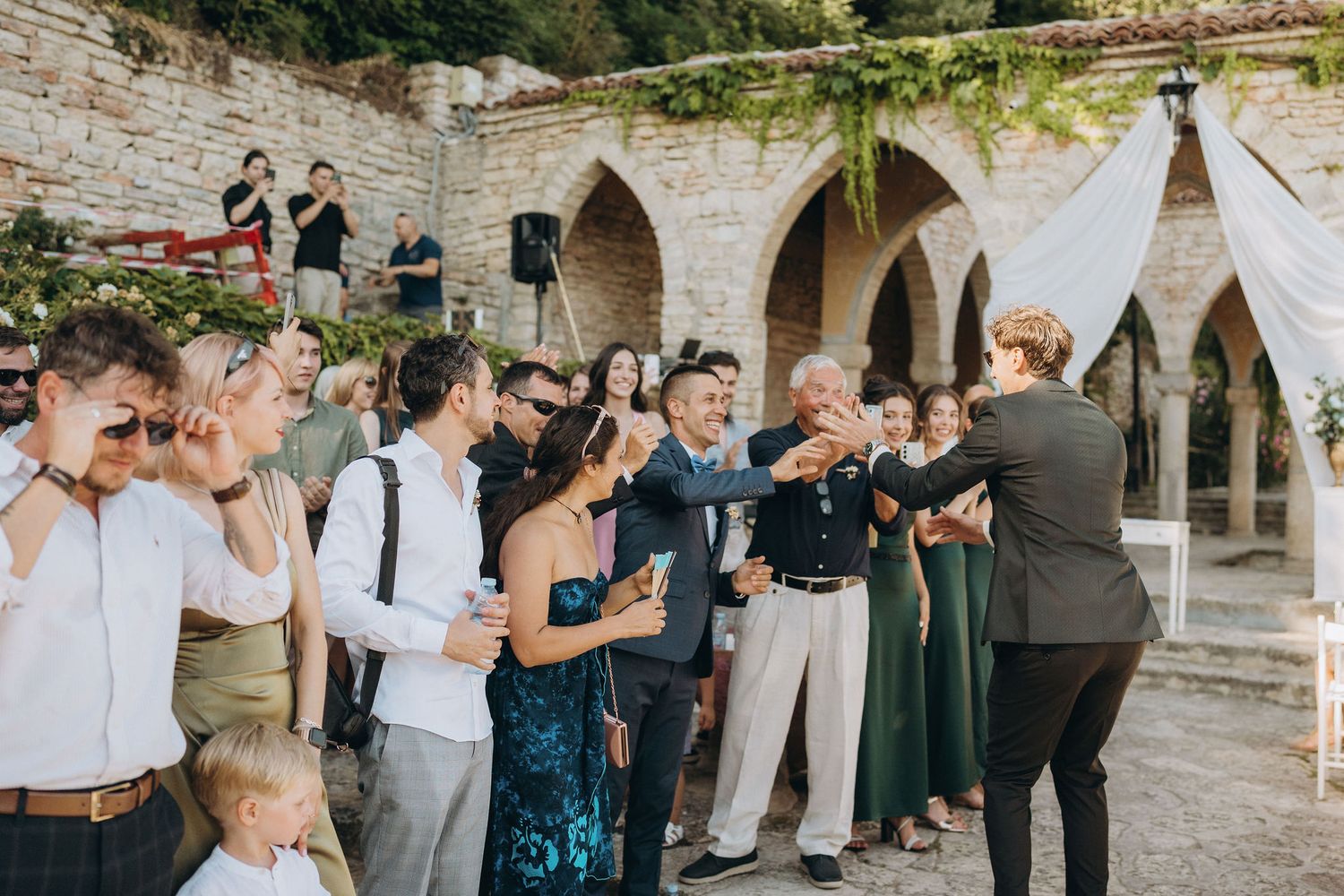 Wedding guests gathered under stone arches enjoying drinks and celebration.