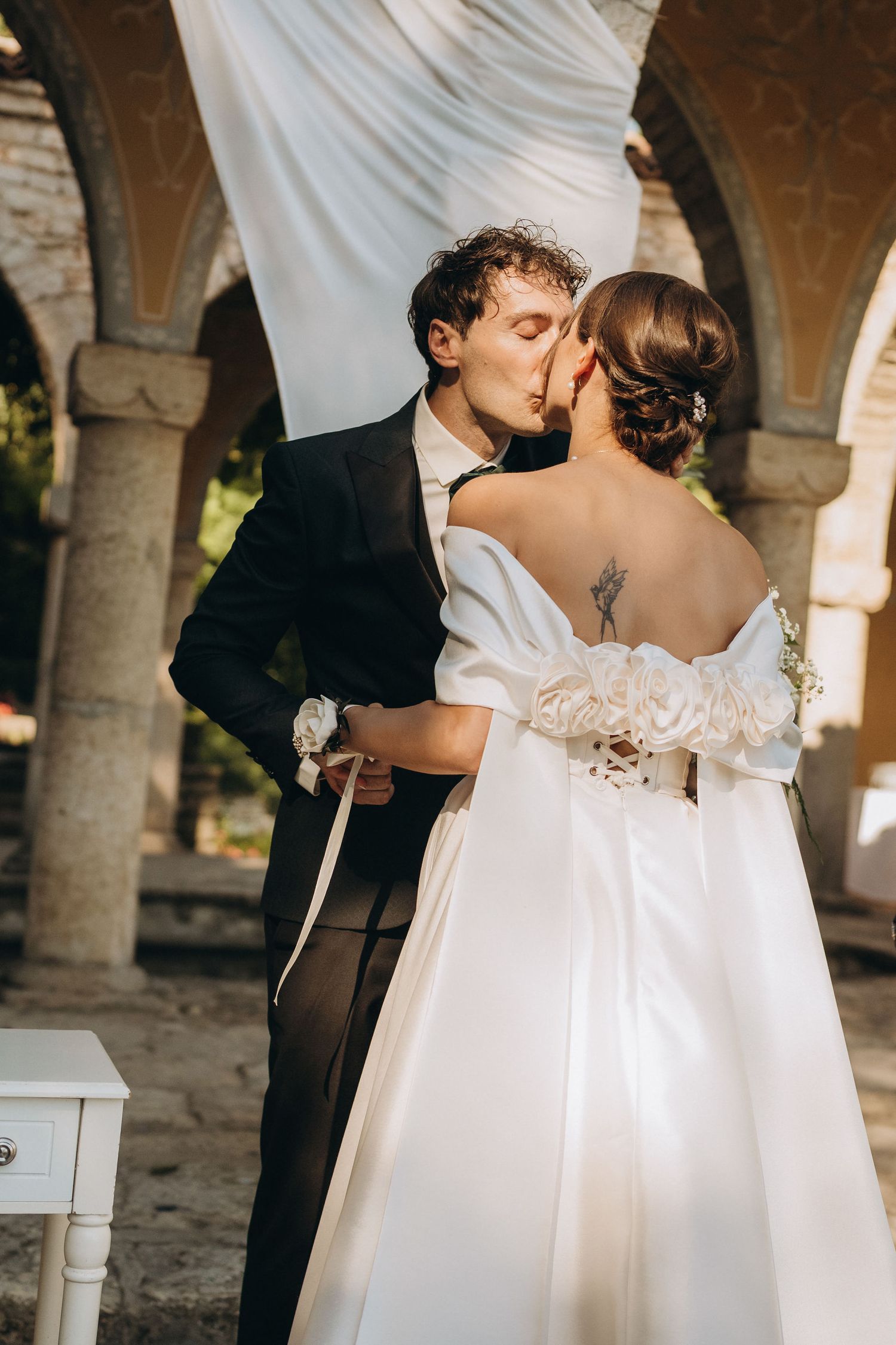 Wedding ceremony taking place under stone archways with flowing white fabric draping the columns.