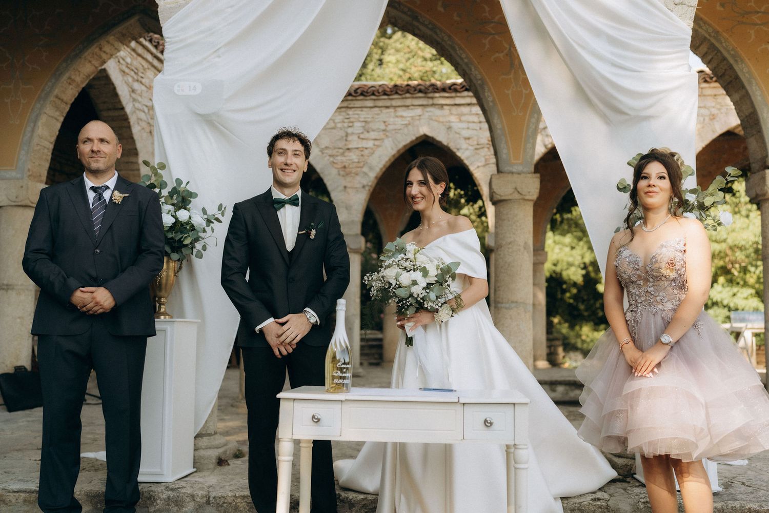 Elegant outdoor wedding ceremony setup with white drapes and stone architecture.