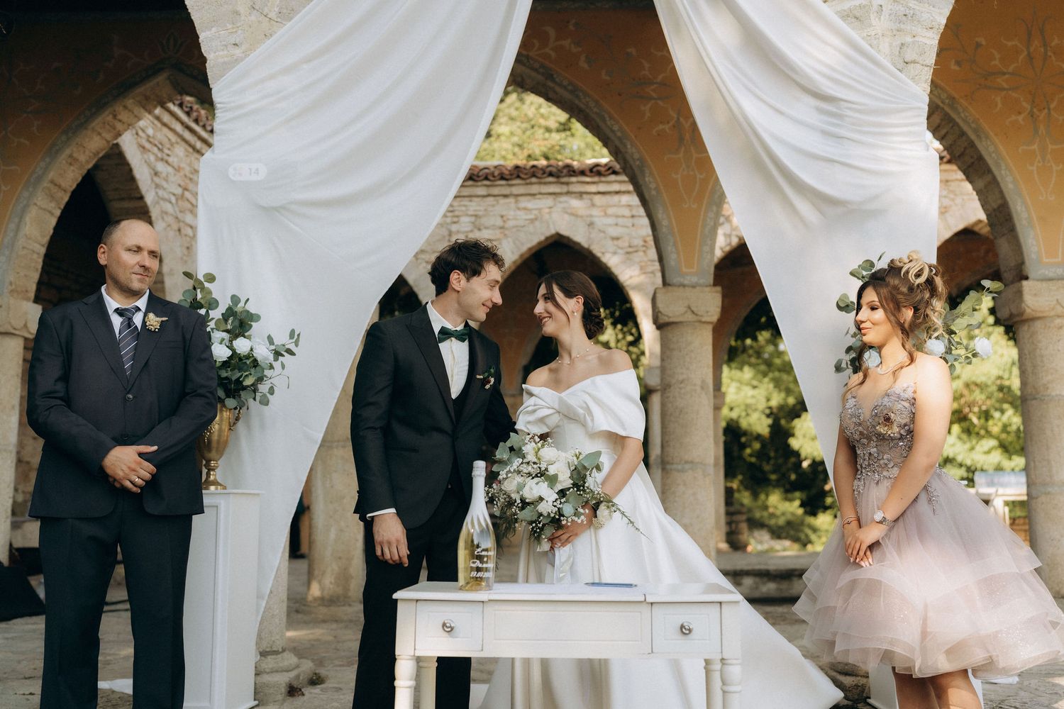Wedding ceremony in a rustic stone colonnade decorated with flowing white fabric.