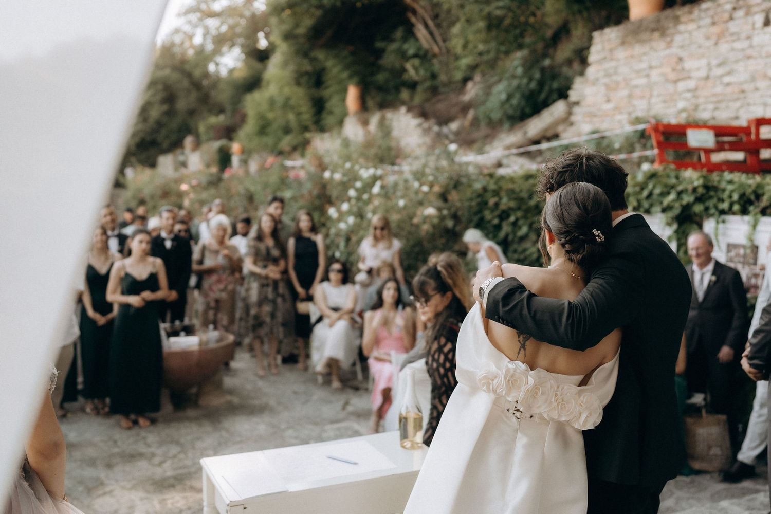 Wedding guests gathered at an outdoor ceremony with stone architecture and natural surroundings.