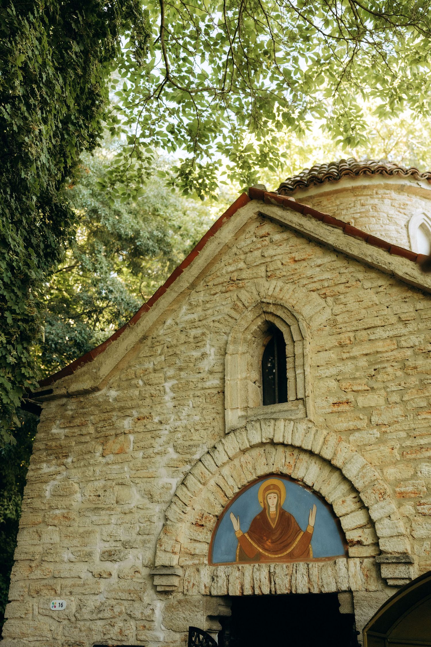 Stone chapel exterior with arched windows and Byzantine-style religious artwork.