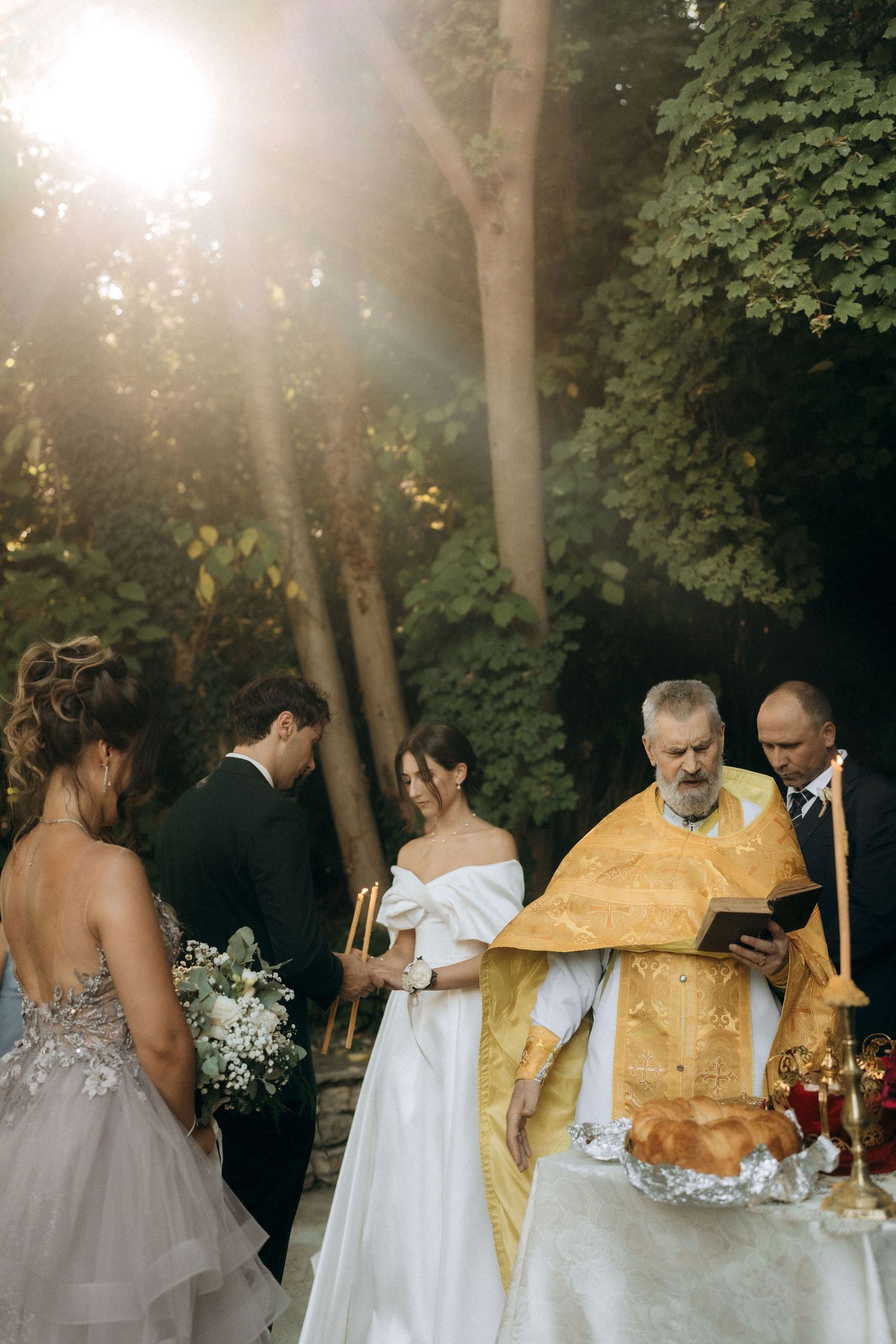 Wedding ceremony at sunset with clergy in traditional gold vestments.