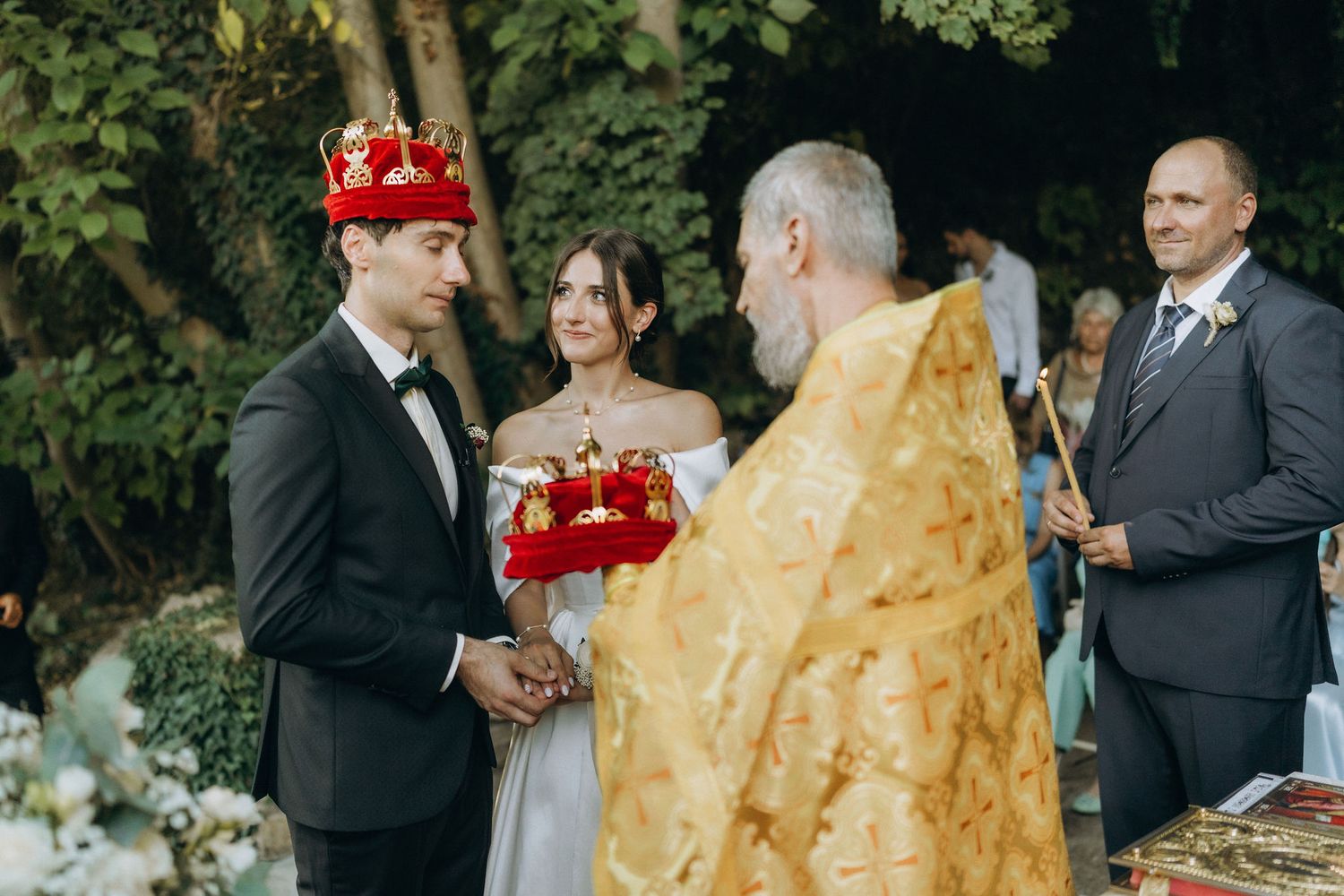 Outdoor wedding celebration with guests in formal attire mingling near stone architecture.