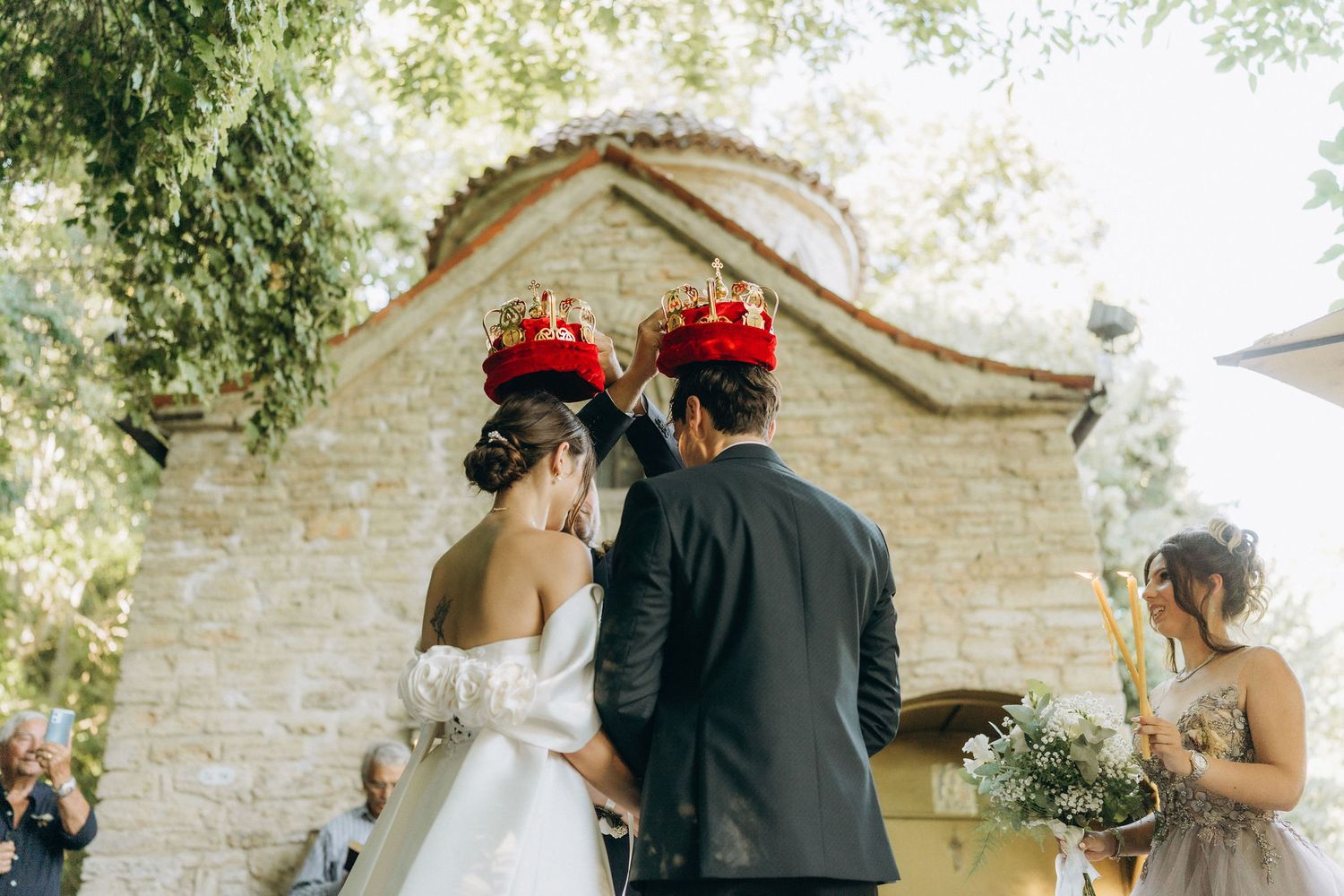 Wedding party gathered for a ceremony outside a historic stone building with arched doorways.