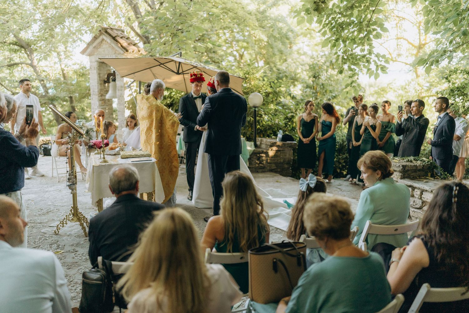 Wedding guests seated outdoors watching ceremony in front of stone chapel.