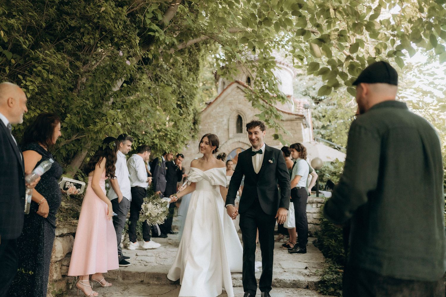 Elegant outdoor wedding ceremony with guests gathered near stone architecture.