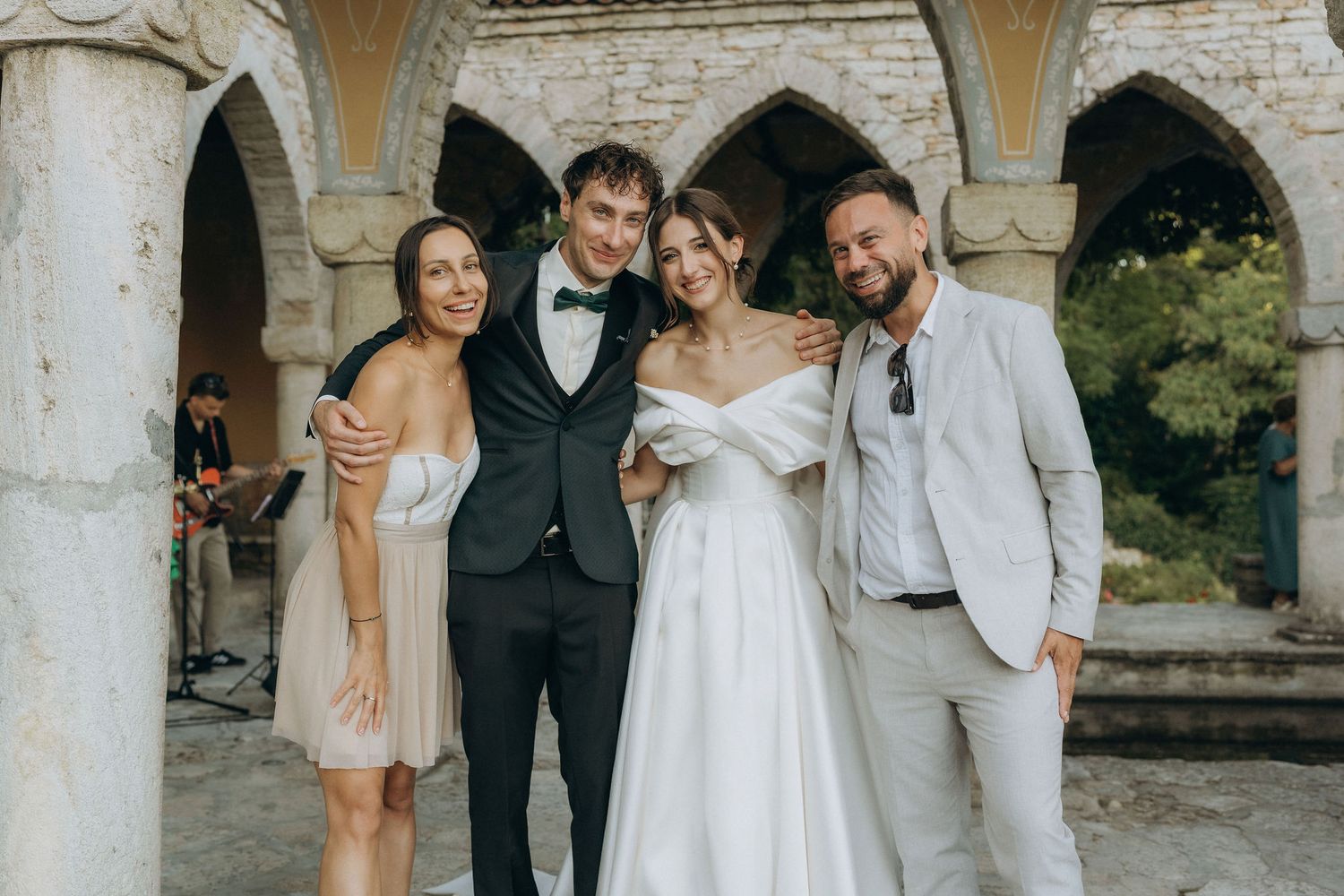 Wedding party posing under stone archways at outdoor venue.