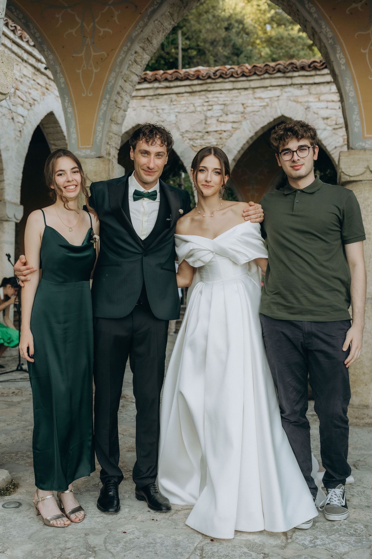 Wedding group photo under stone arches with formal attire.