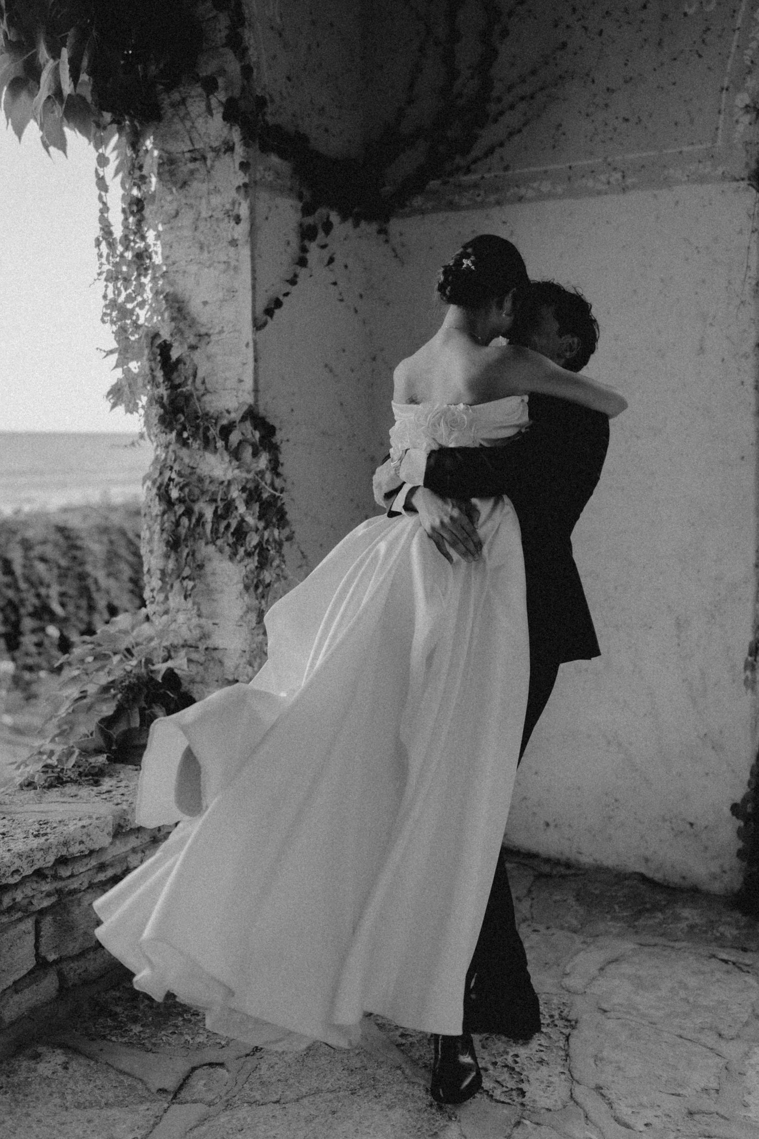 Black and white photo of a couple dancing in an elegant stone courtyard.