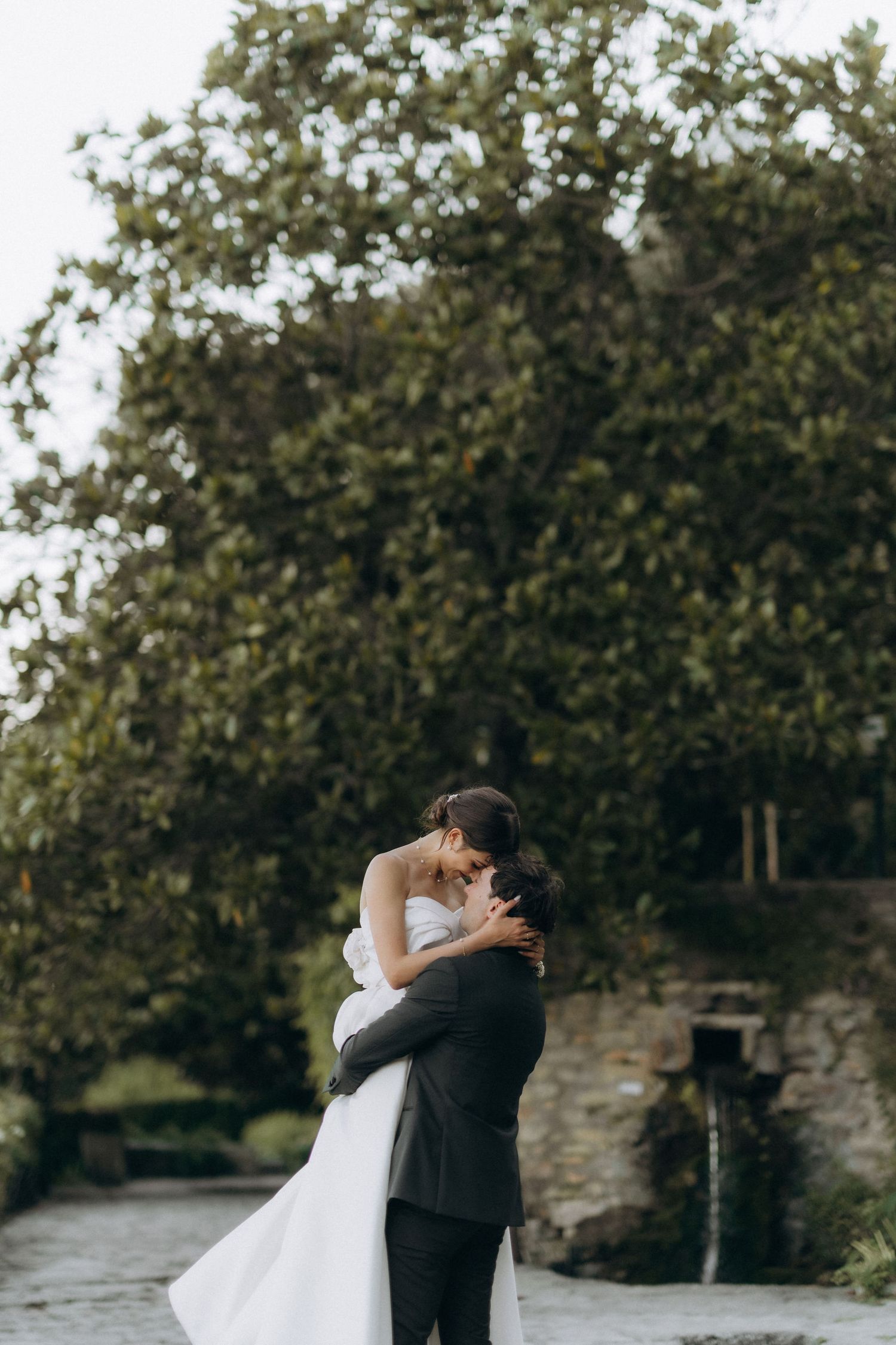 Romantic wedding couple embracing on stone pathway surrounded by lush garden scenery.