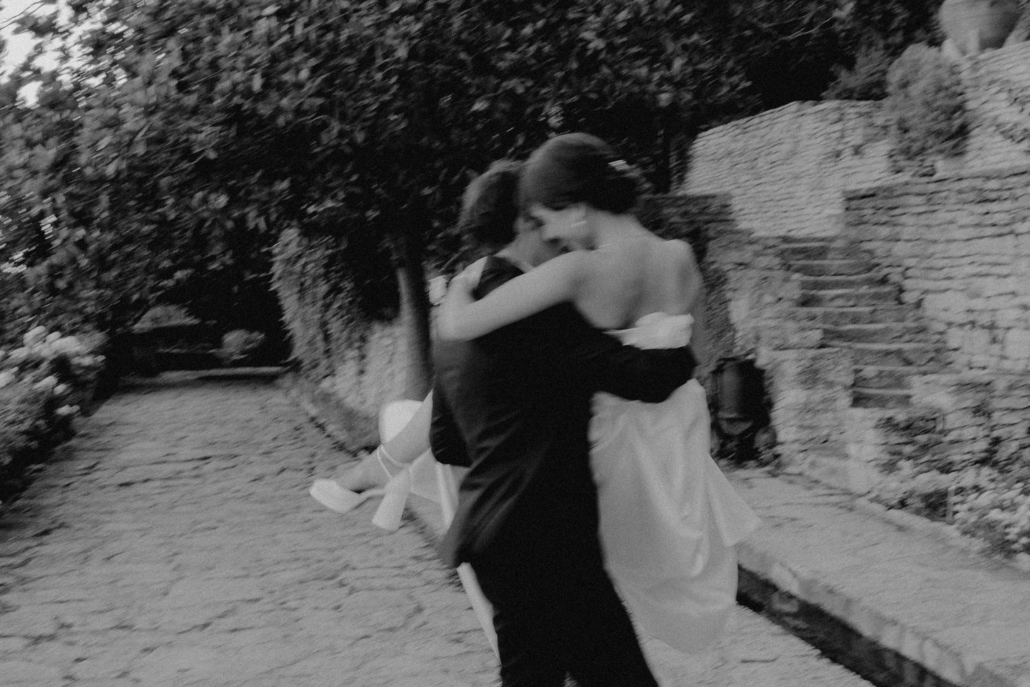Black and white photo of couple dancing together on garden path.