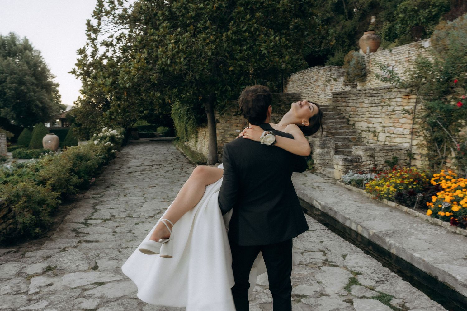 Wedding couple sharing playful moment on stone walkway surrounded by garden walls.