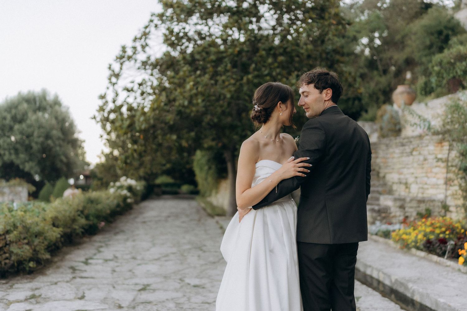Intimate wedding portrait of couple embracing on garden pathway with stone walls.