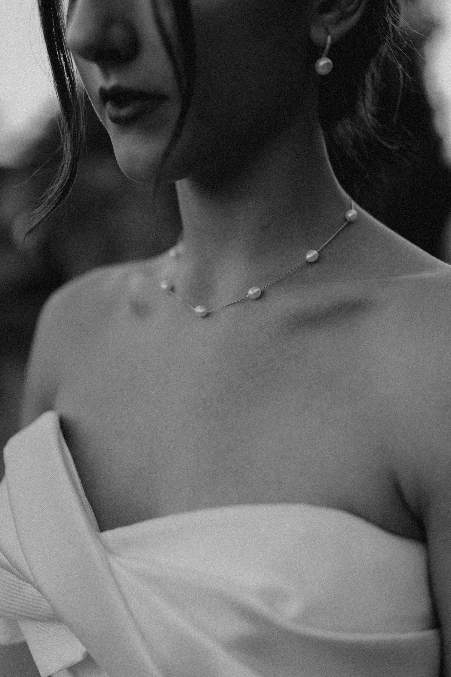 Close-up black and white detail of delicate pearl necklace and strapless wedding dress.