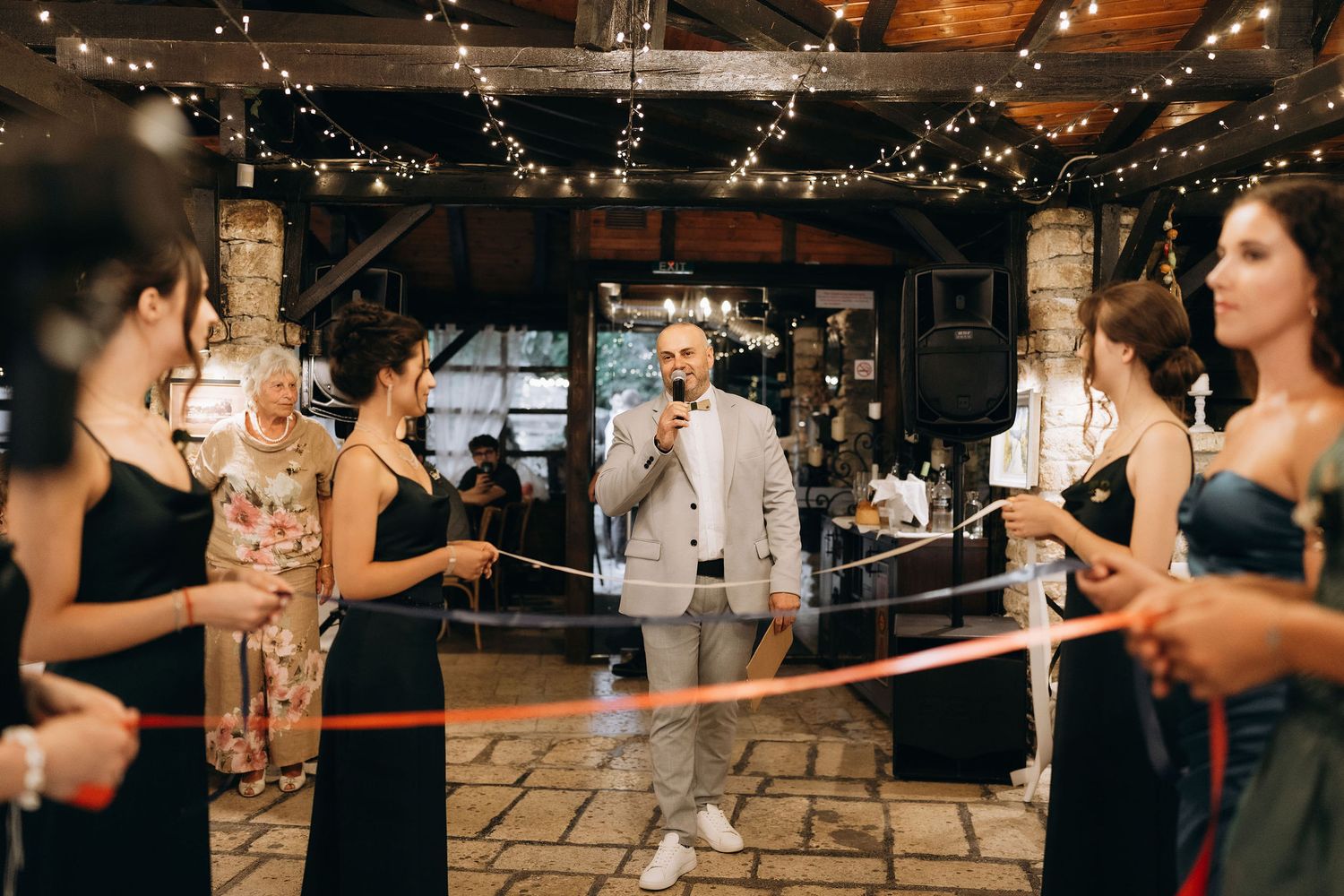 A celebration at an indoor venue decorated with string lights as guests gather around during a special moment.