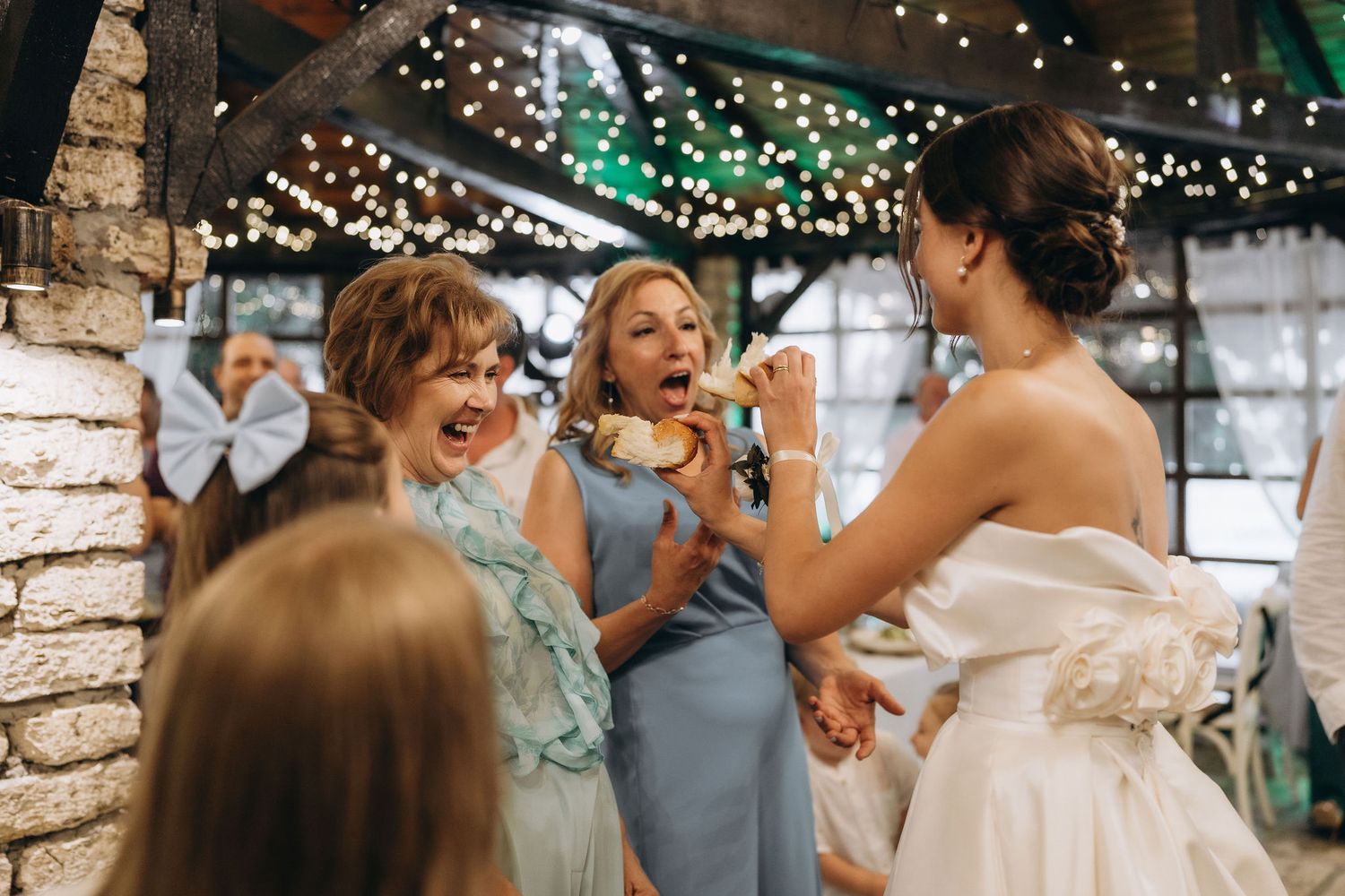 Joyful celebration moment at a wedding reception with string lights and brick walls.