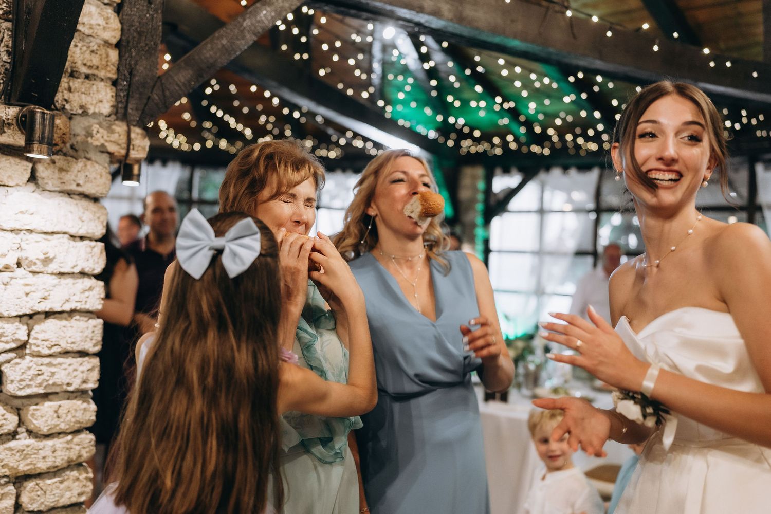 Guests share laughter and smiles during a wedding reception under twinkling lights.