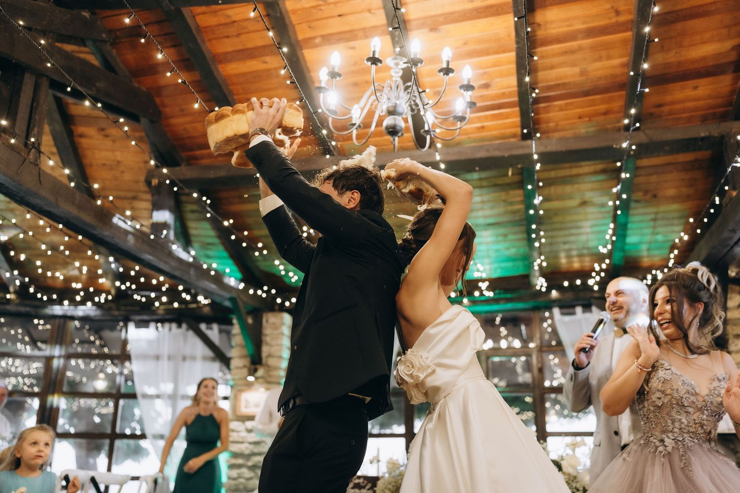 Dancing and celebration at a wedding reception under wooden beams with string lights.
