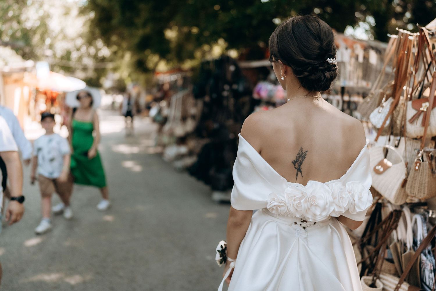 Wedding party walking through a sunny outdoor market with decorative hanging items.