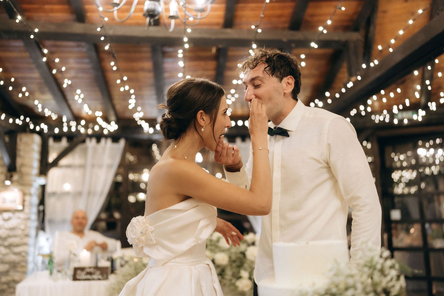 Wedding celebration under wooden beams with twinkling string lights creating a romantic atmosphere.