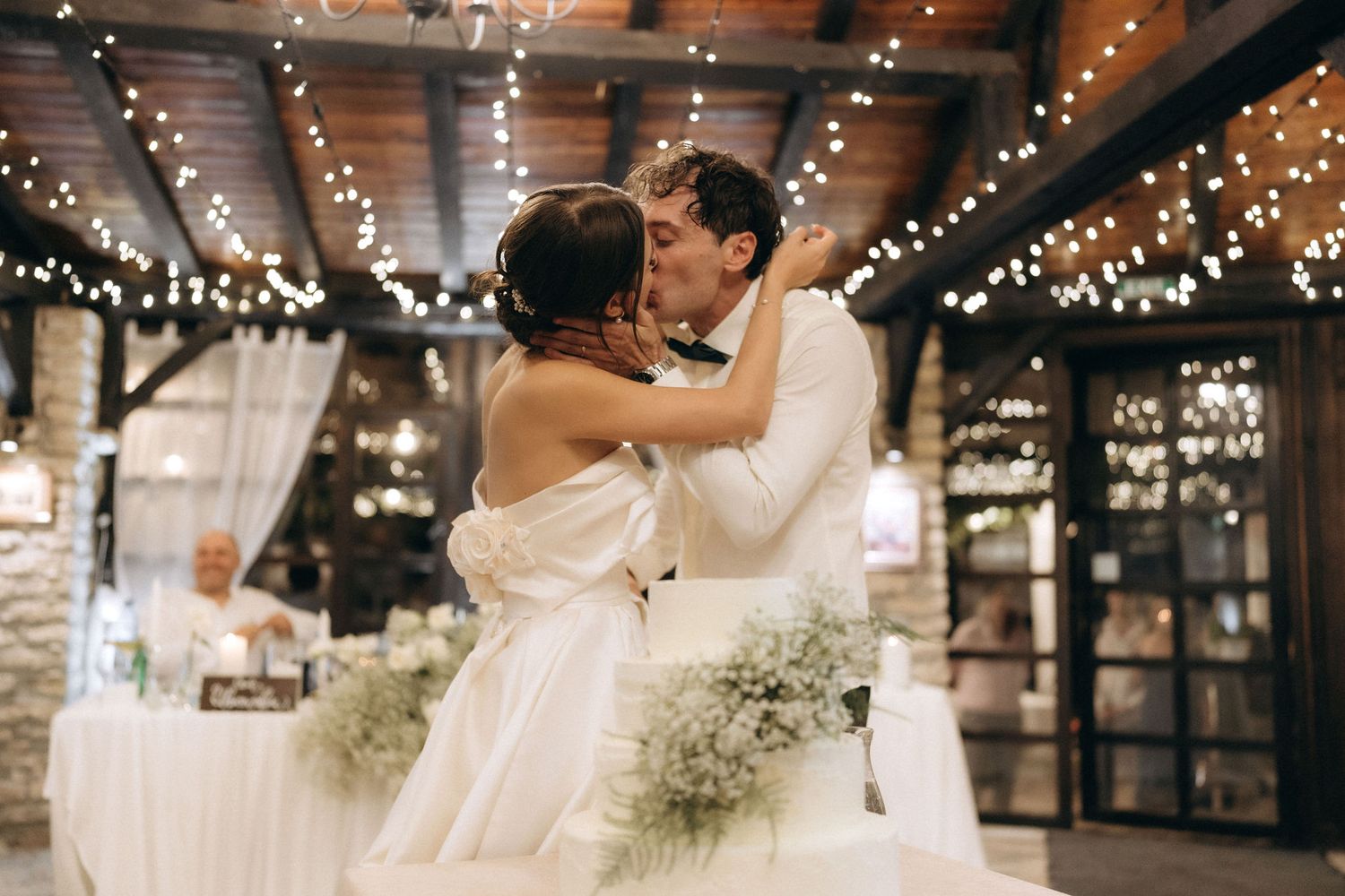 Romantic dance moment captured under rustic wooden beams and string lights.