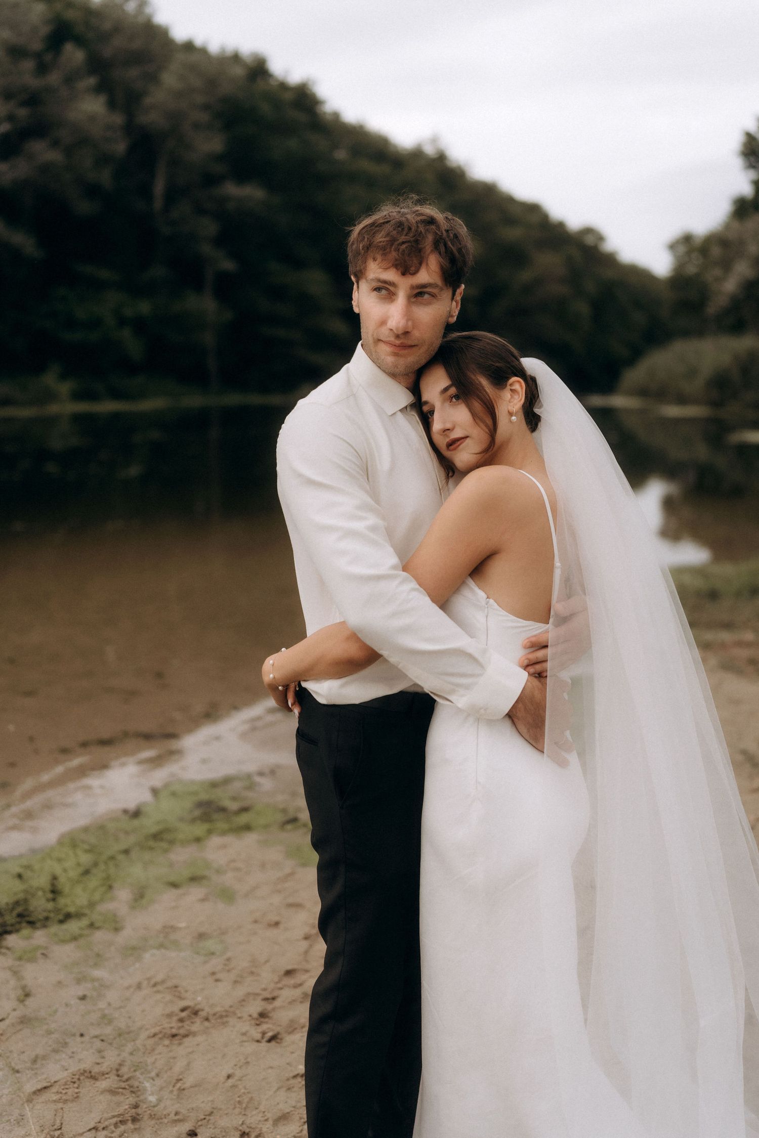 Romantic wedding photos captured on a lakeside beach with natural lighting.