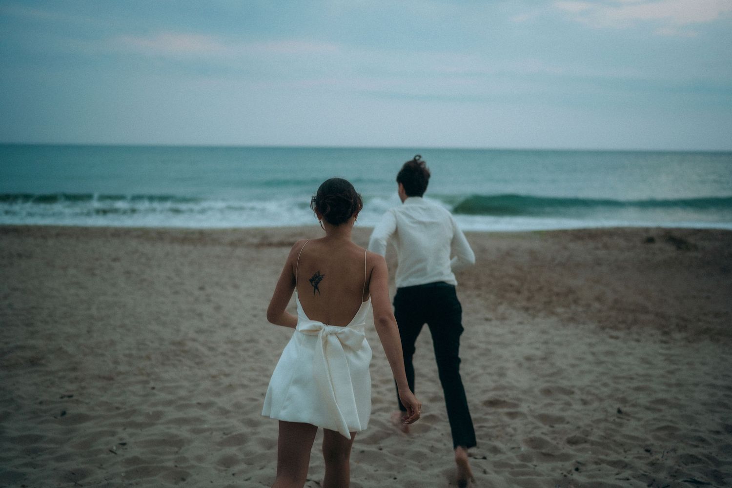 Couple walking hand in hand along shoreline during beach engagement session.