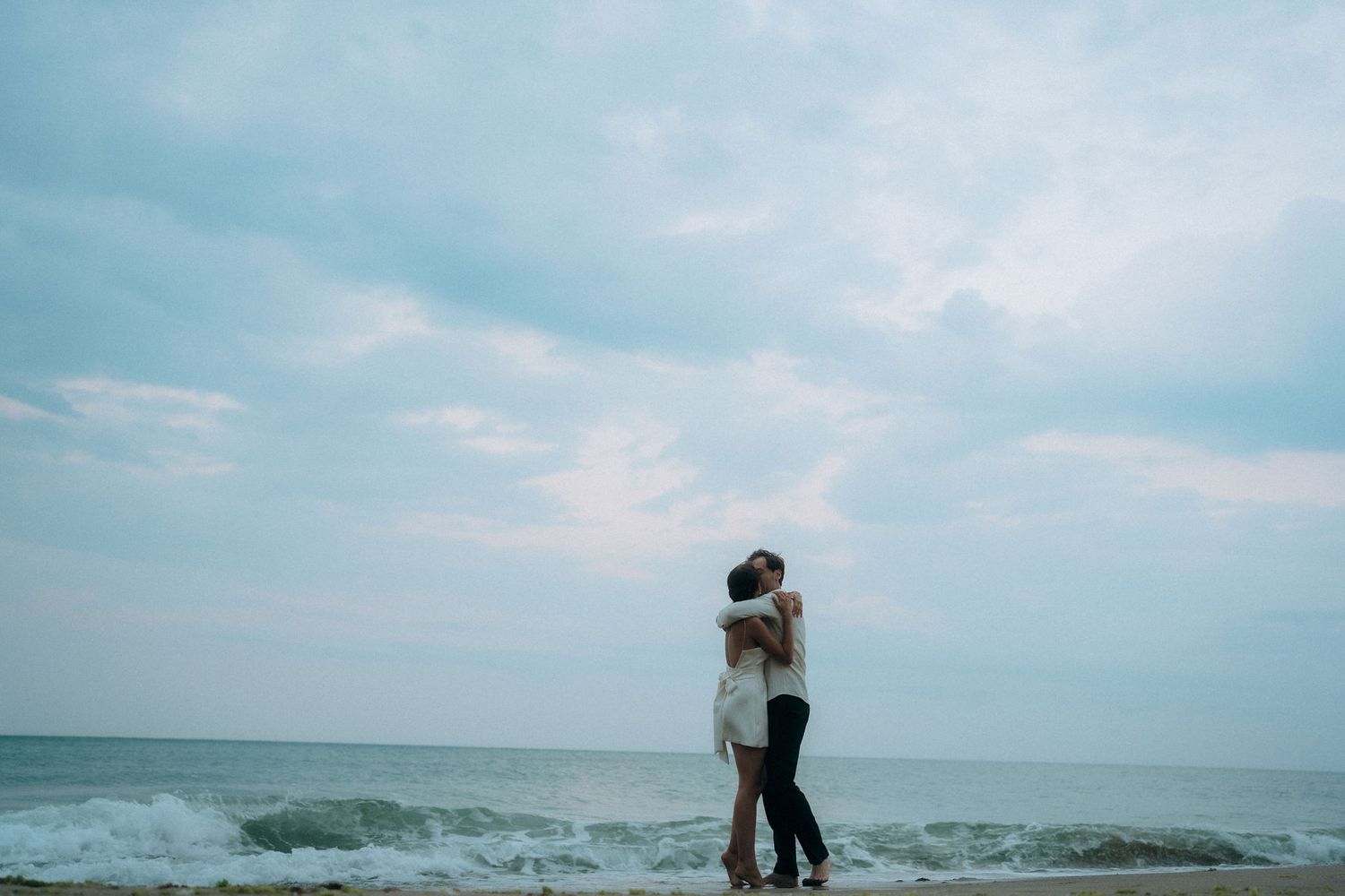 Romantic couple embracing on a moody beach with waves crashing in the background.