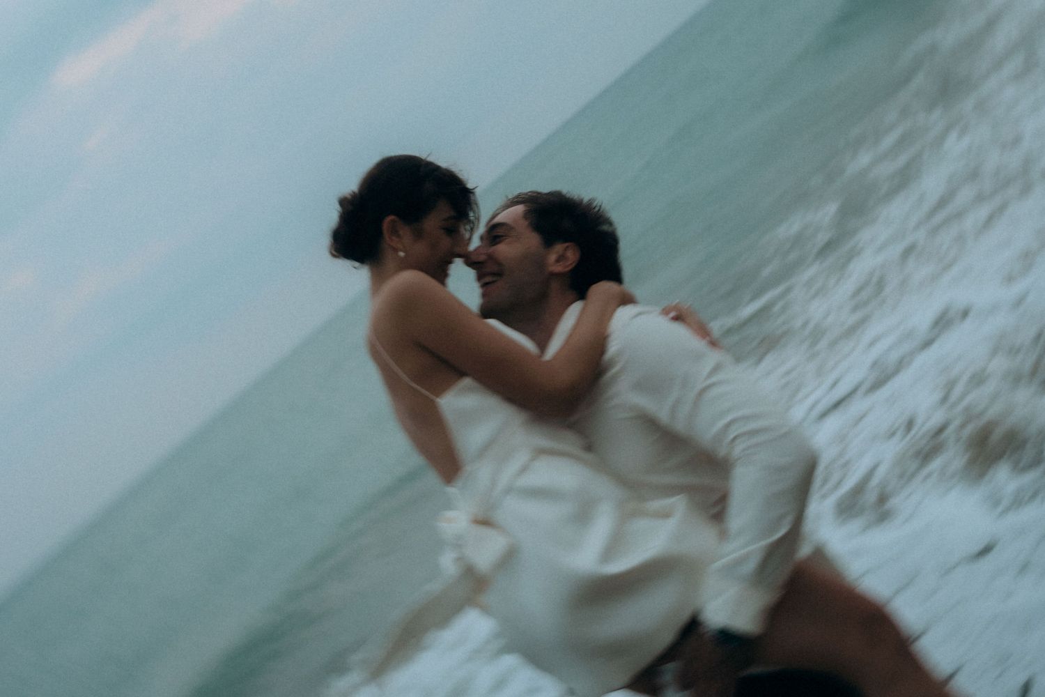 Intimate beachside moment between couple with dramatic ocean waves in background.