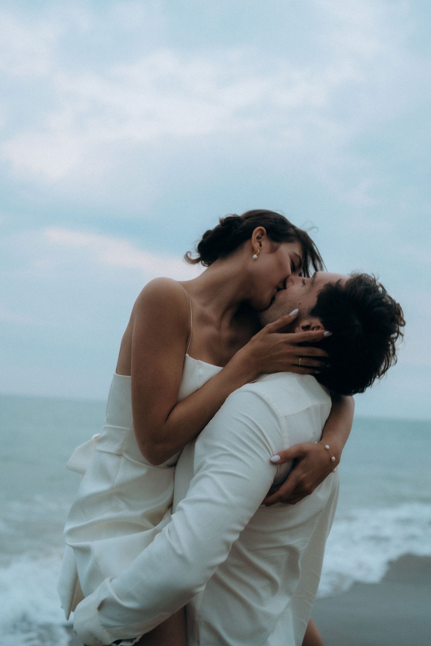 Passionate embrace between couple in white clothing on windswept beach.