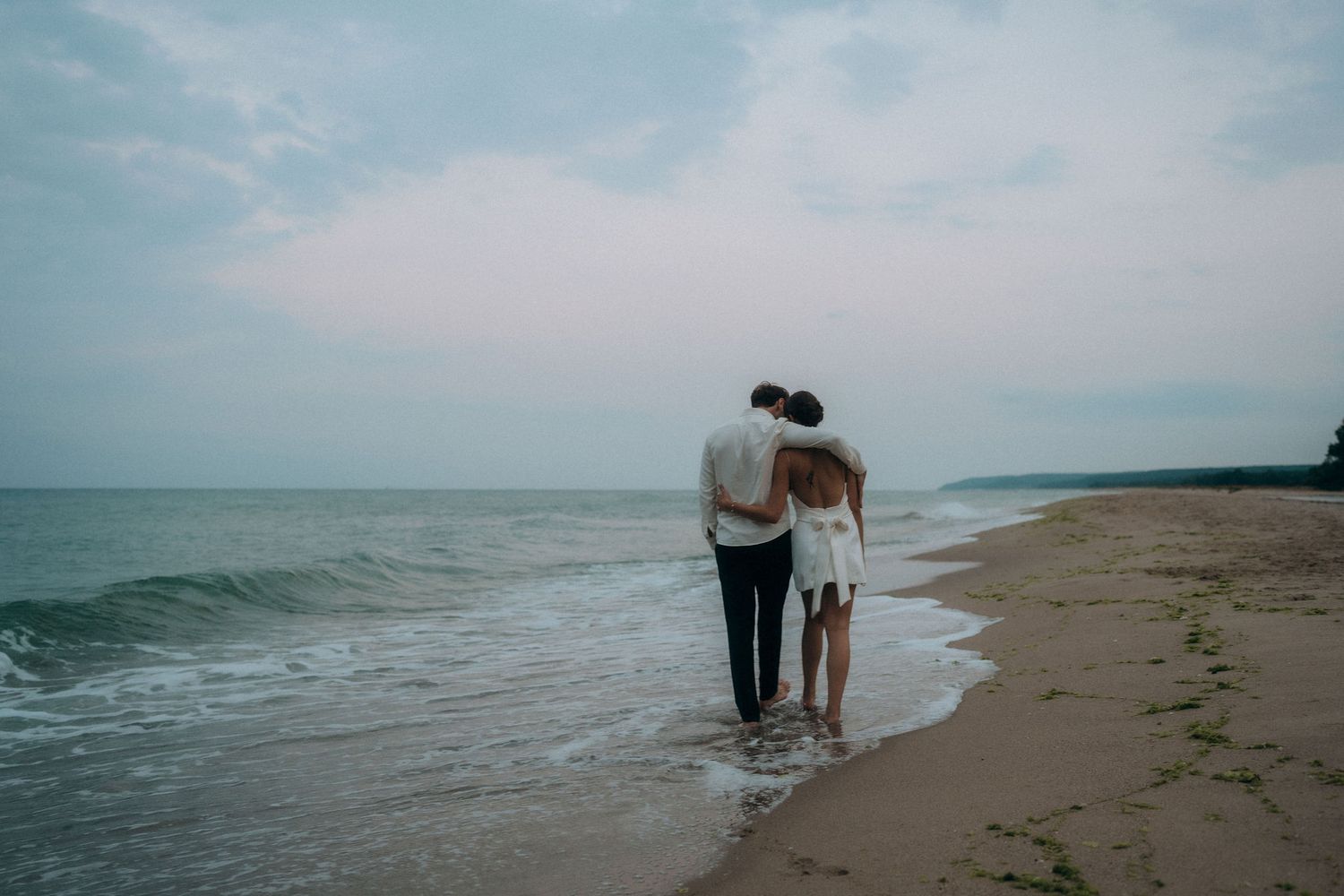 A couple walking together along the shoreline at dusk with waves rolling in.