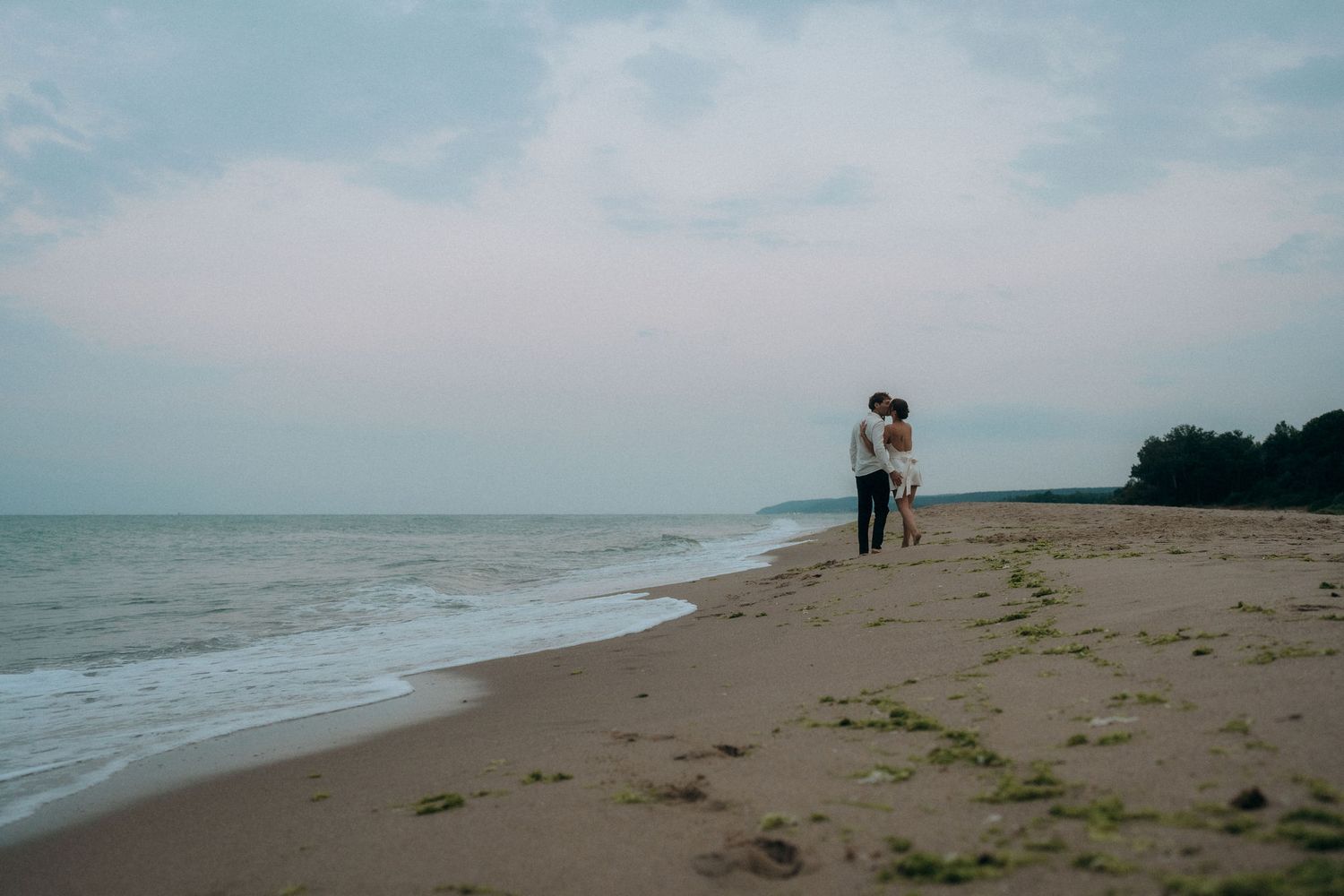 Silhouetted couple standing together on an empty beach during sunset.