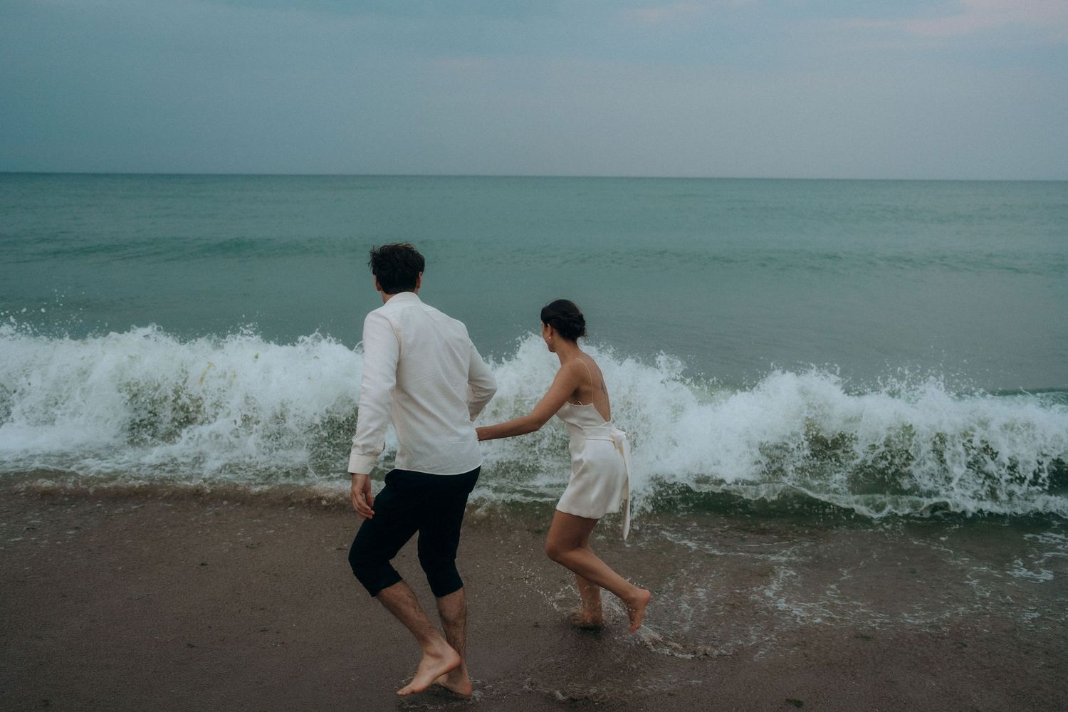 Couple splashing in the ocean waves during a beach photoshoot.