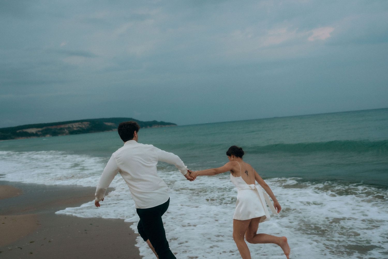 Playful couple running away from incoming waves on a sandy beach.
