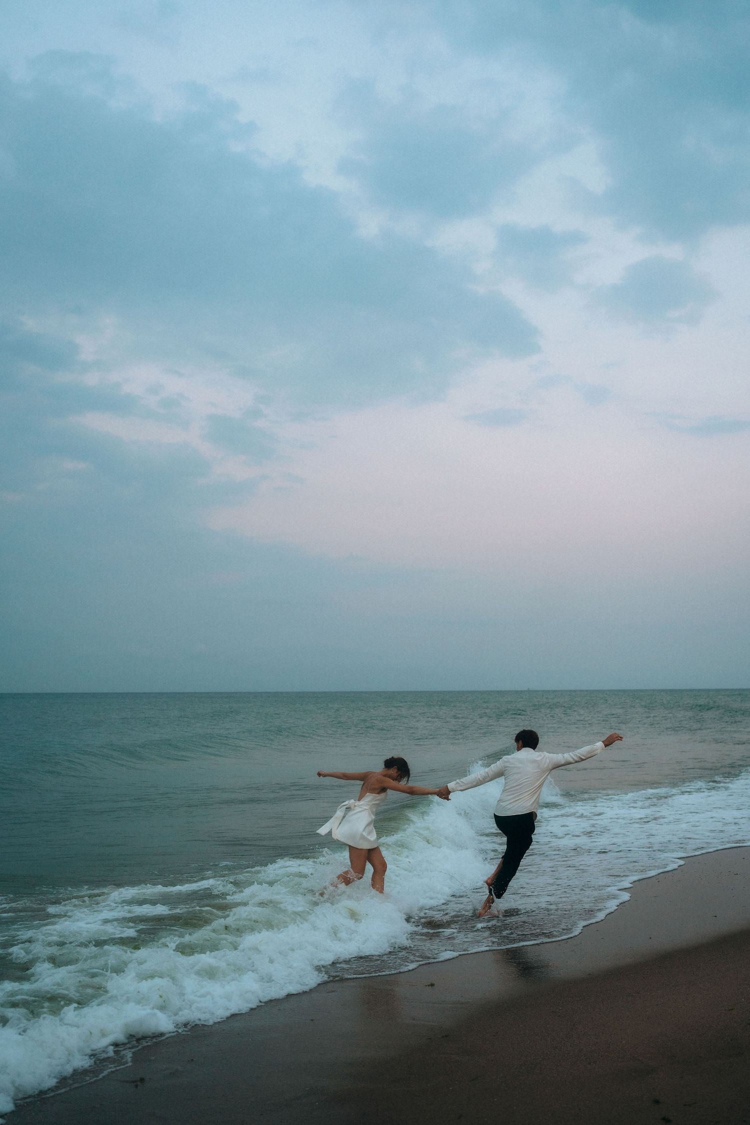 Joyful couple leaping together through ocean waves at the beach.