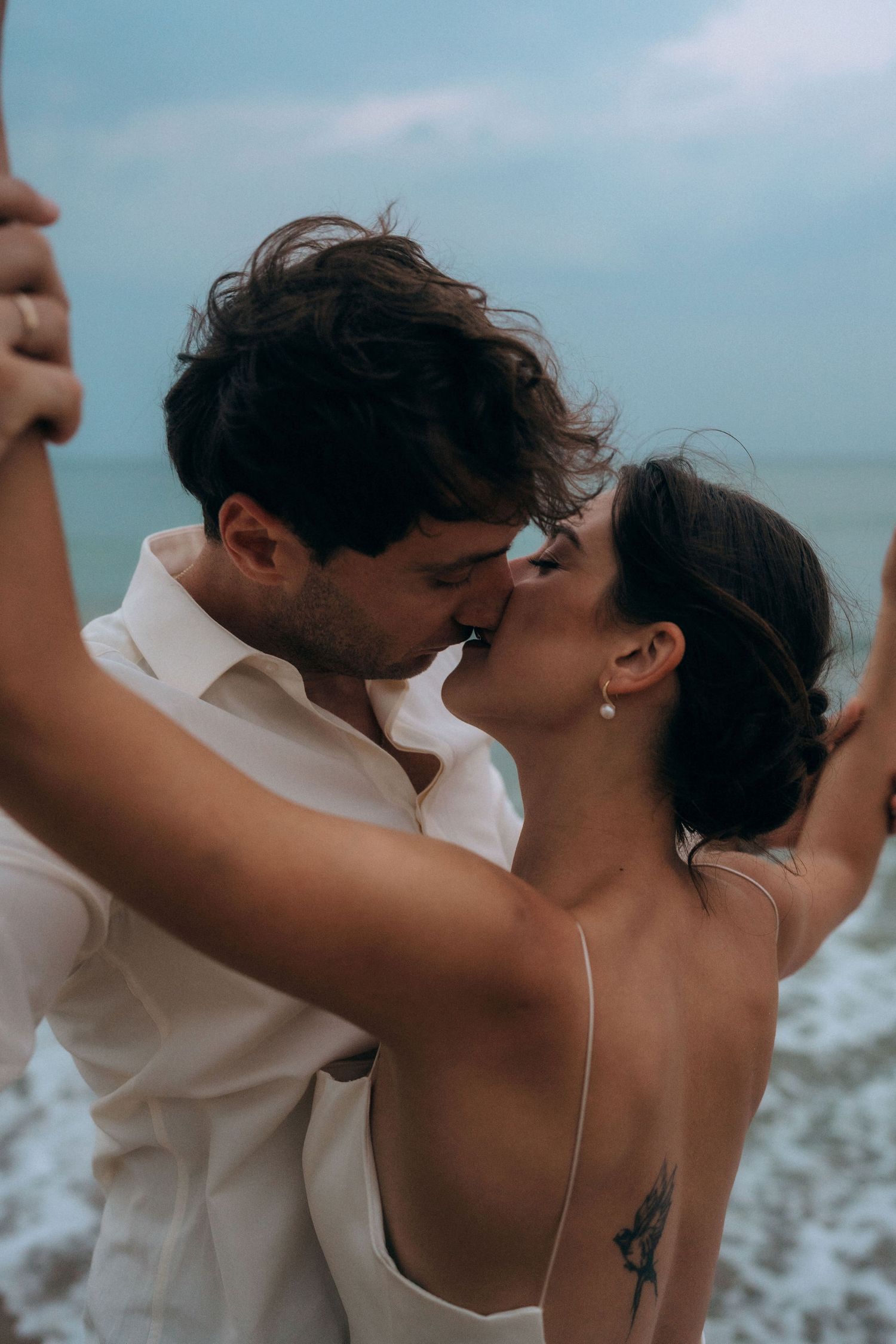 A couple shares an intimate moment on the beach in wedding attire.