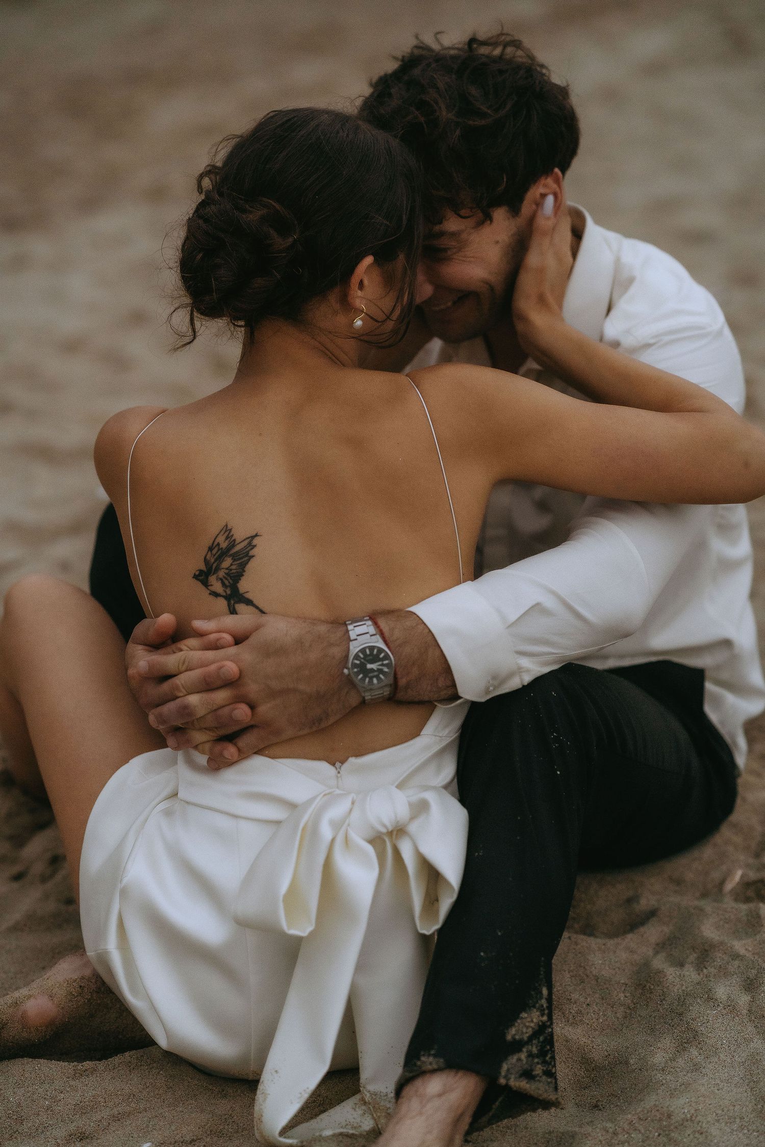 An intimate beach portrait session showing a couple sitting close together on the sand.