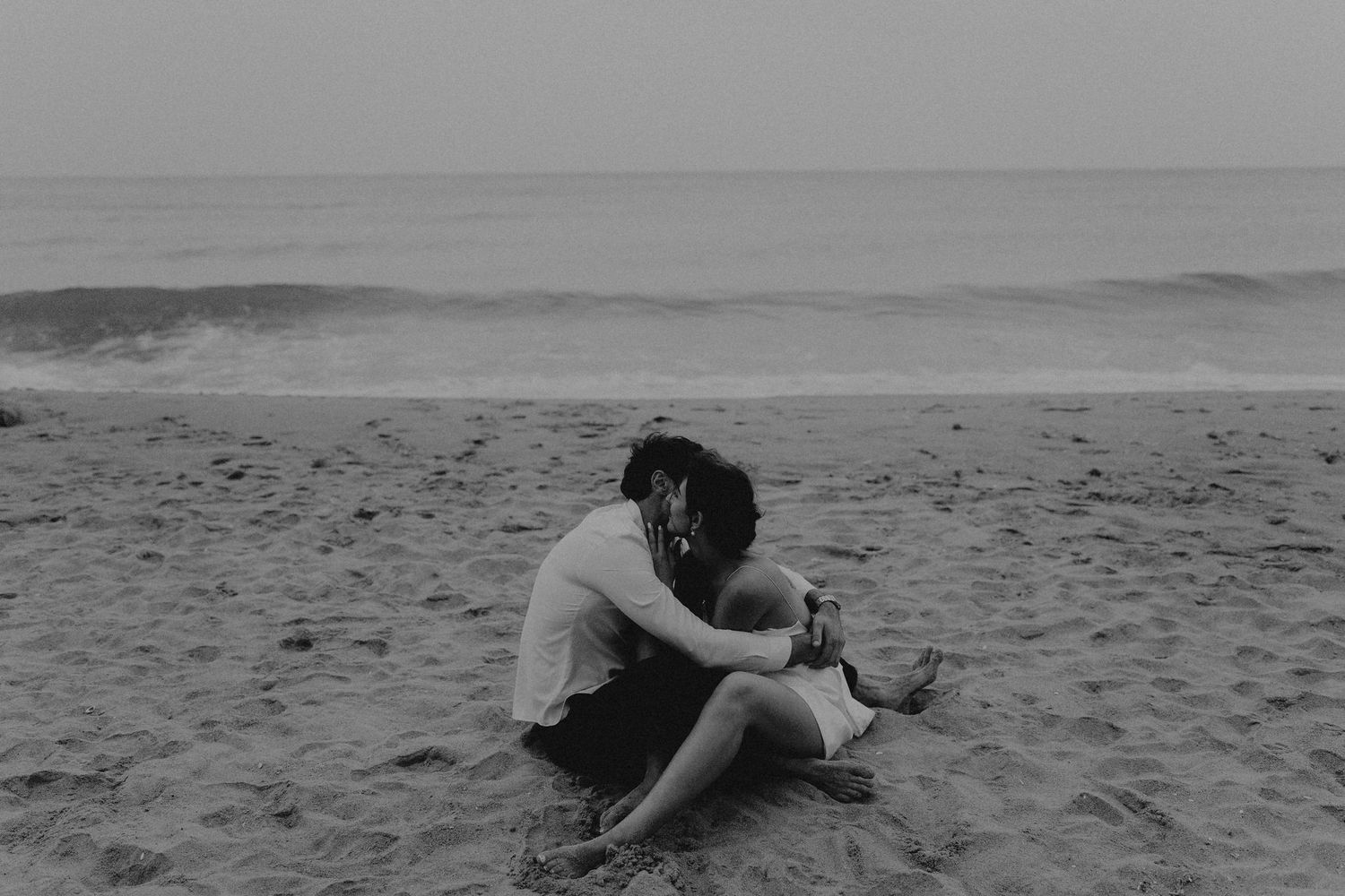A black and white beach photo capturing intimate moments between a couple.
