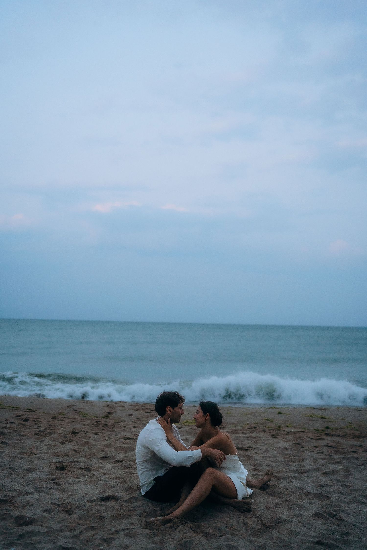 A couple relaxes on the beach sand as ocean waves crash in the background.