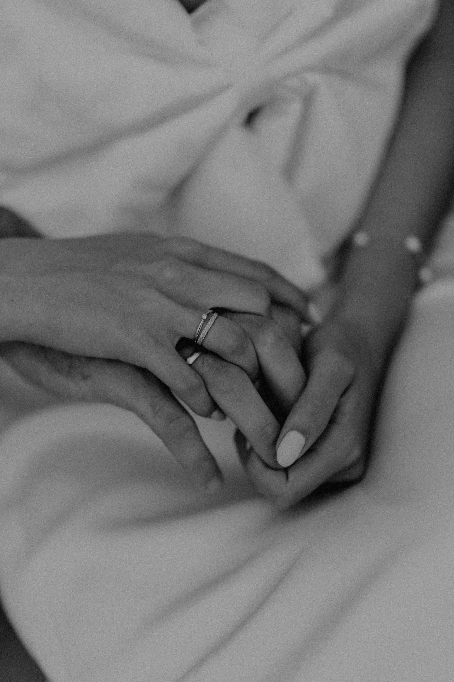 Close-up of intertwined hands with wedding rings in black and white.