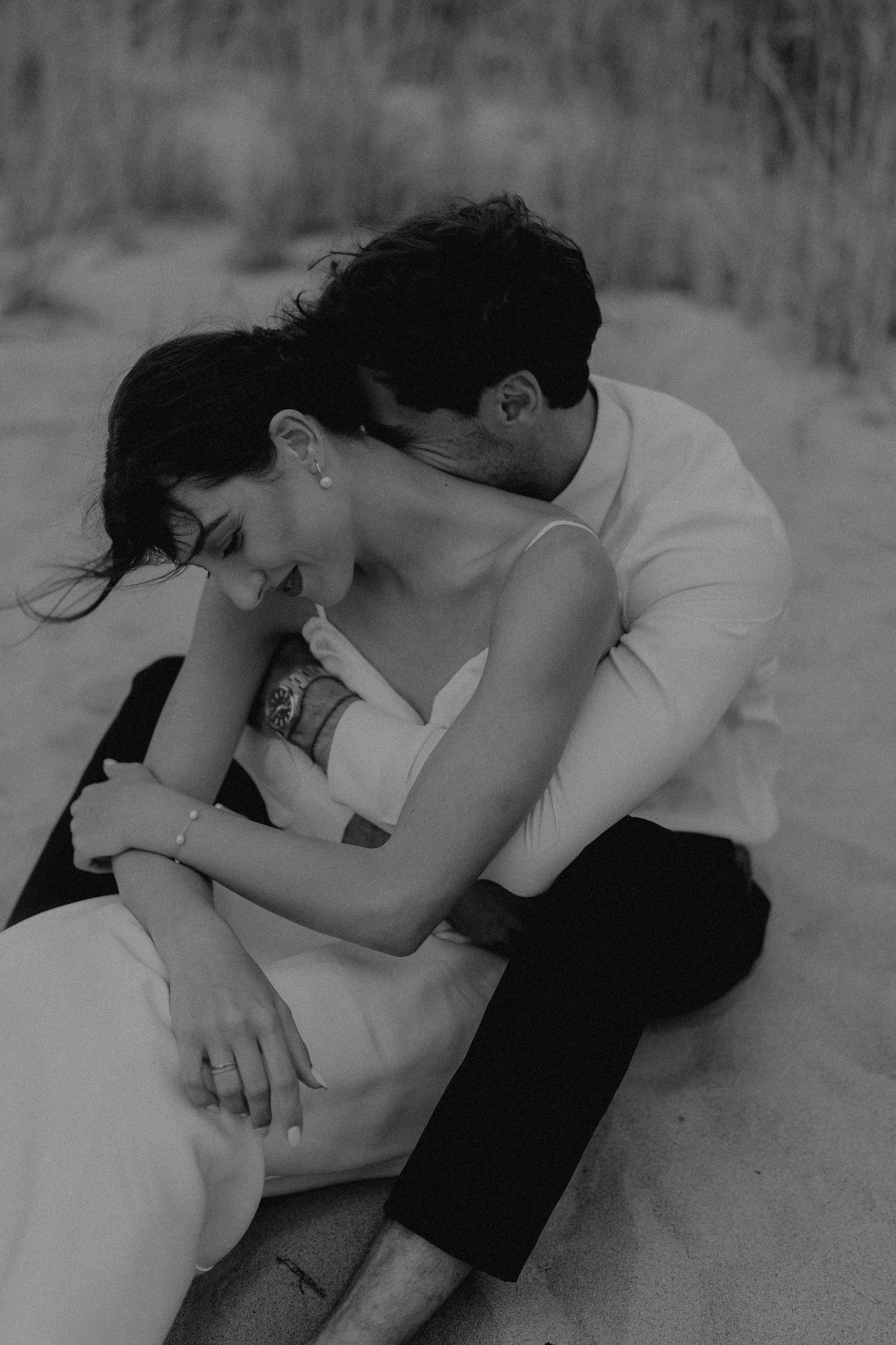 Intimate black and white portrait of couple laying in beach sand.