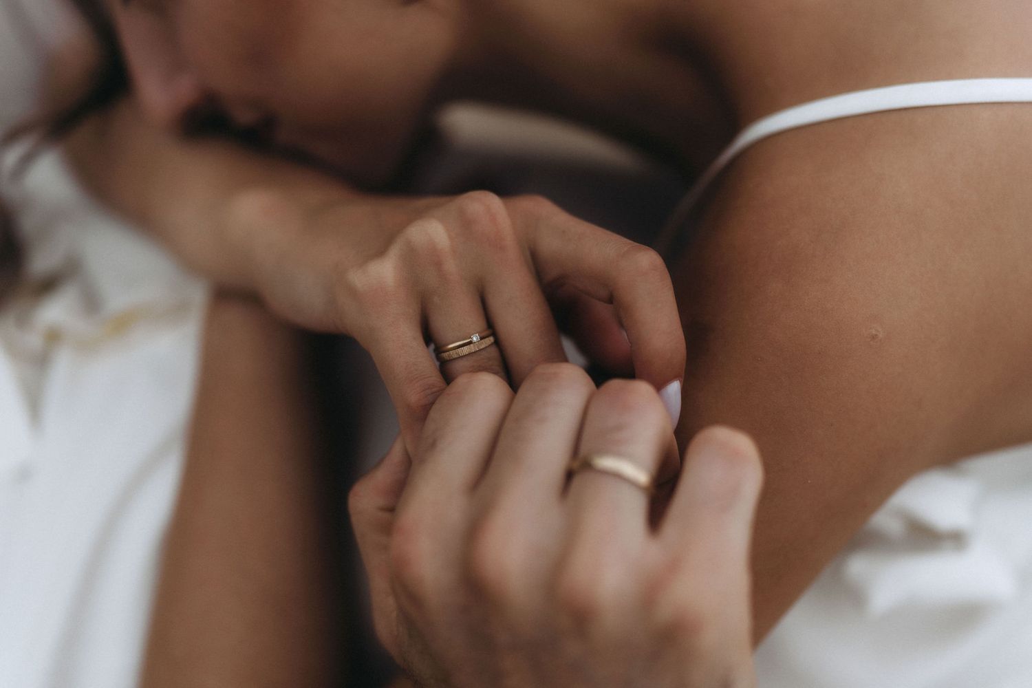 Intimate detail shot of hands and rings against soft white fabric.