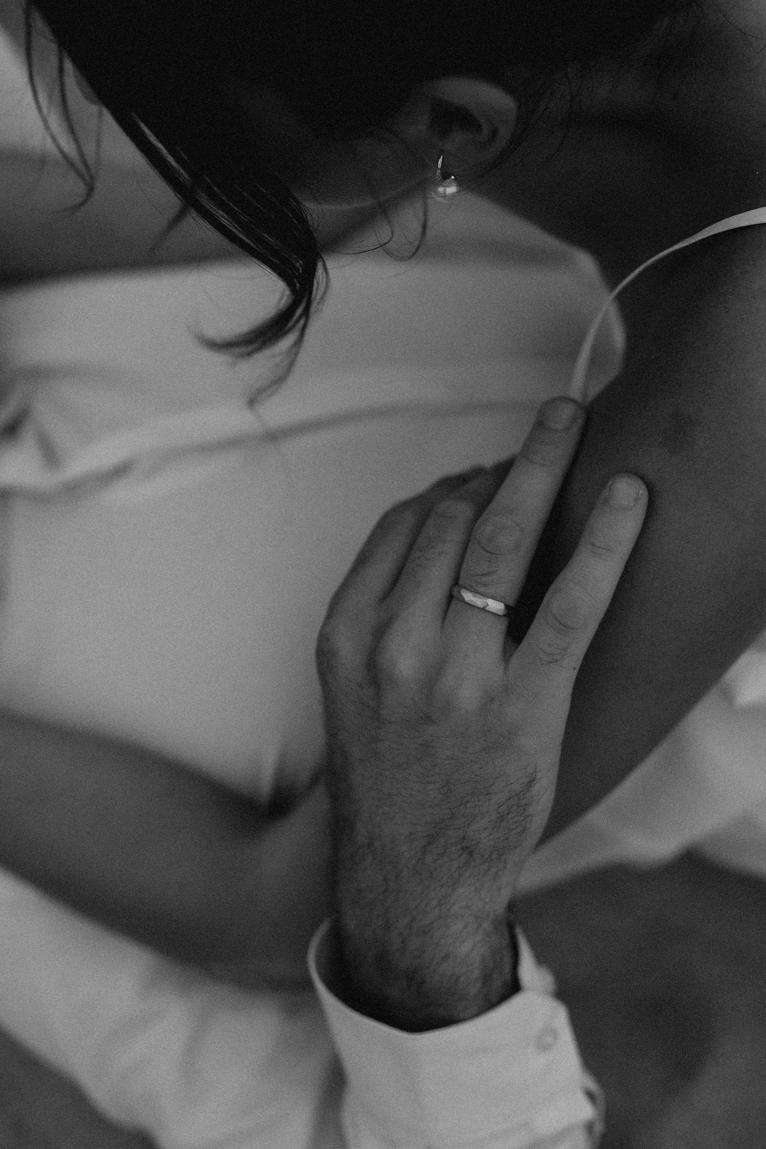 Black and white close-up of gentle hand touches and wedding rings.