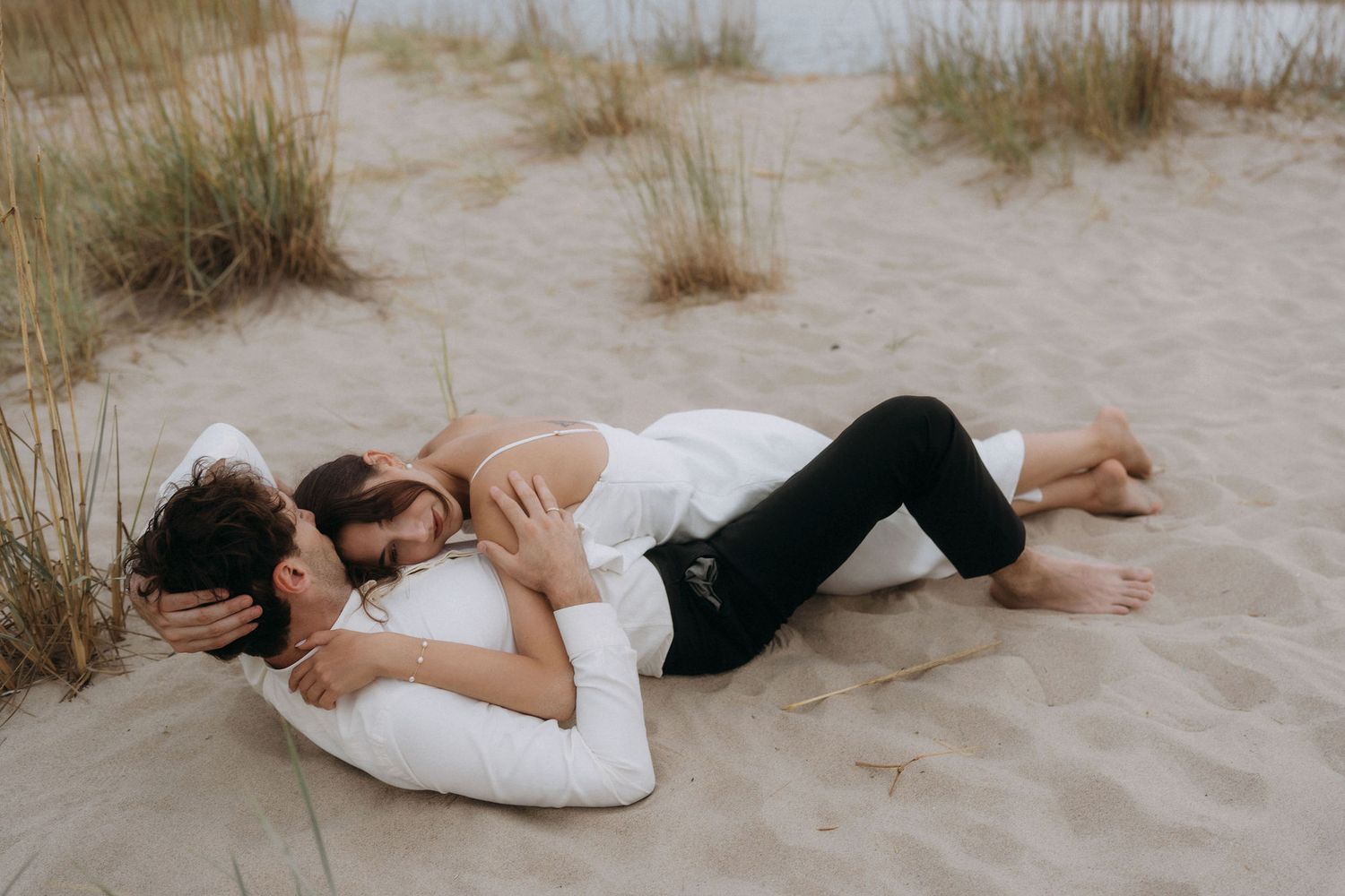 Romantic couple lying together on sandy beach during sunset photoshoot.