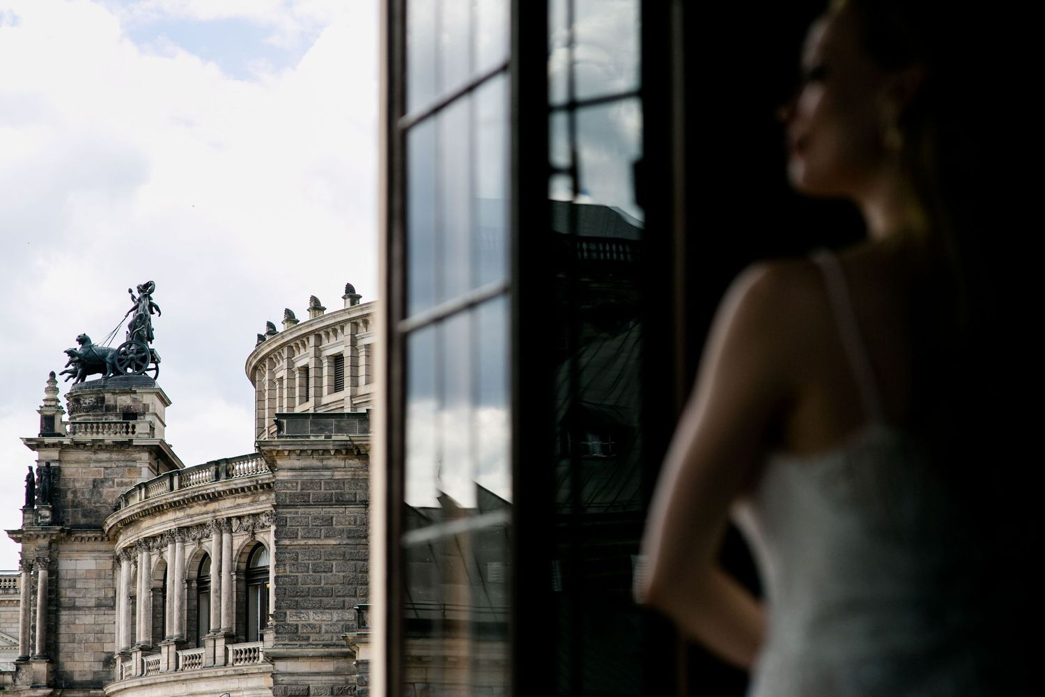 Through a window frame, a silhouetted figure gazes at historic Dresden architecture with ornate baroque details.