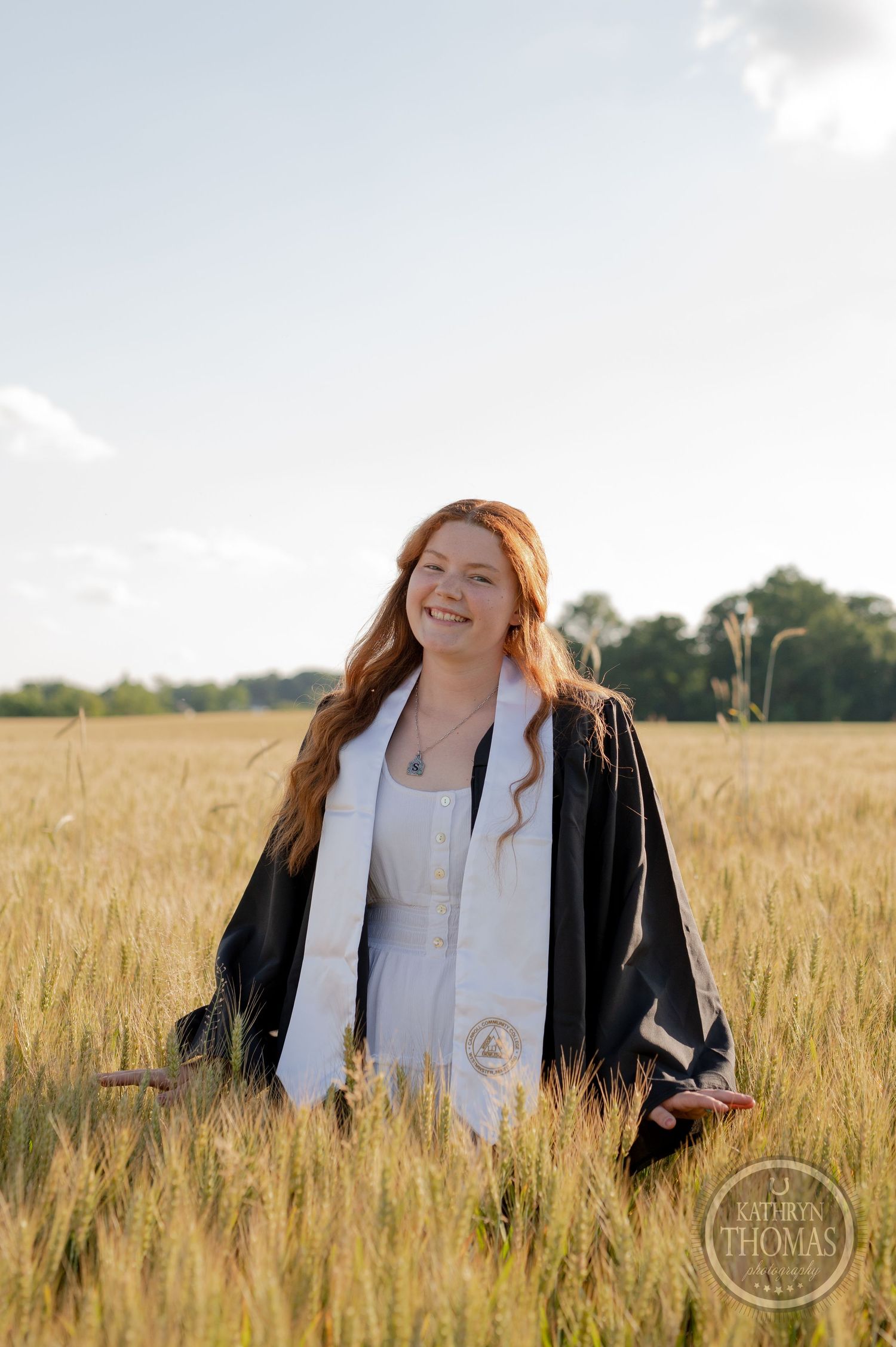Graduate stands joyfully among tall wheat stalks at golden hour.