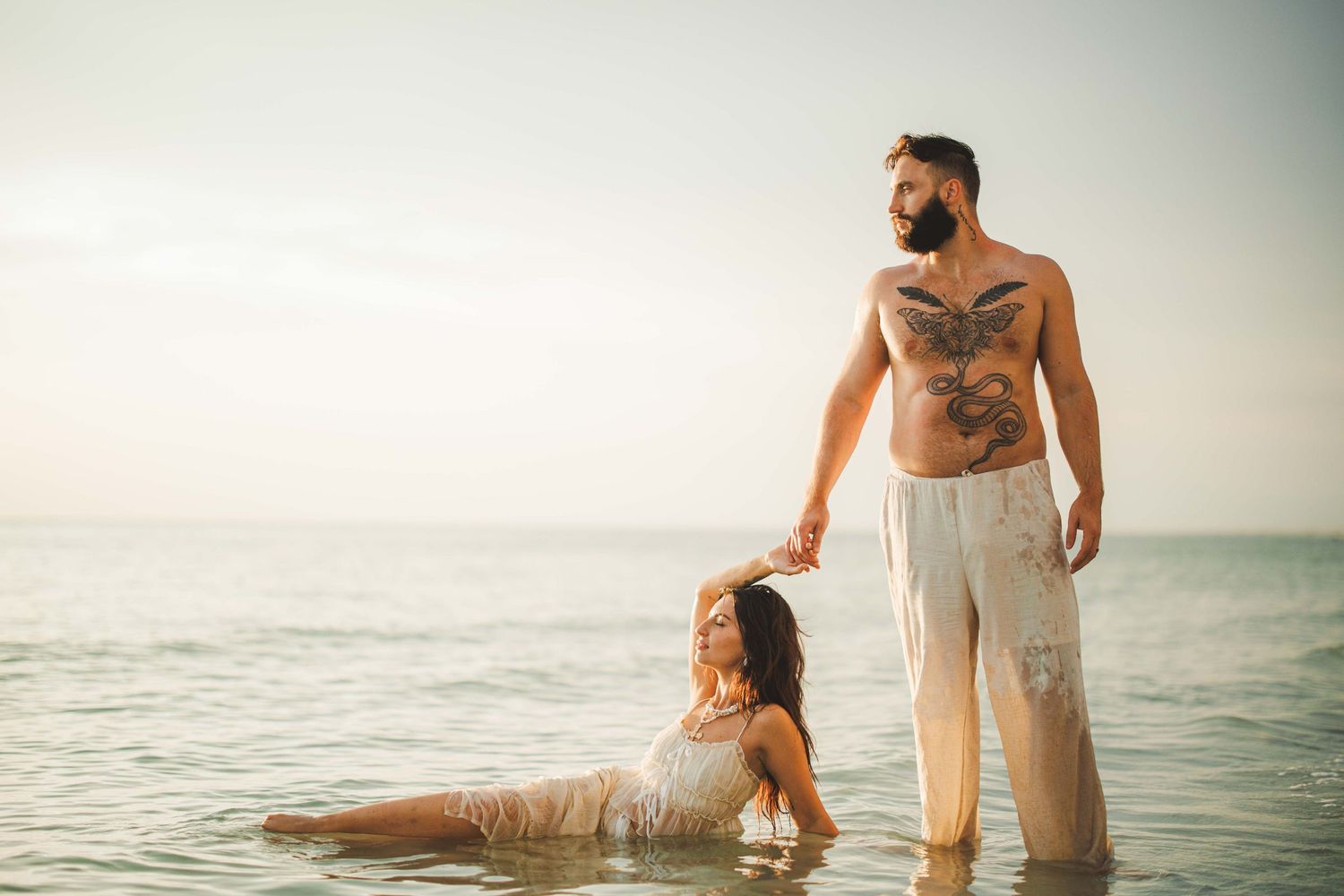 A couple plays in the ocean water during a beach photoshoot at sunset.