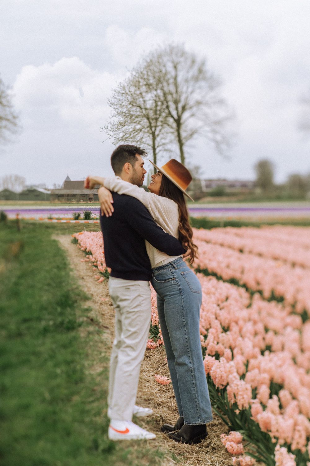 Couple sharing an intimate moment among rows of pink tulips in a Dutch countryside field.